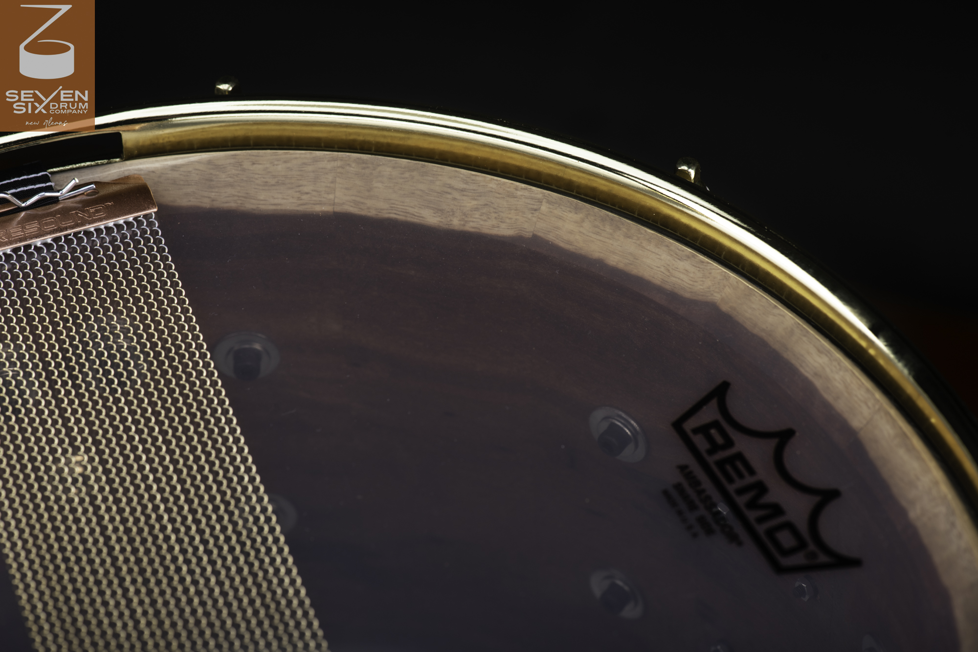 Handmade dark wood snare drum with a polished brass hoop, clear resonant head, and coiled snare wires.