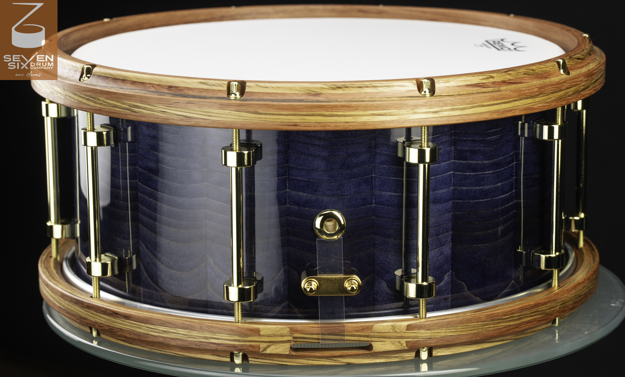 Handmade snare drum with a glossy blue stained wood shell, layered natural wood hoops, and gold tube lugs.