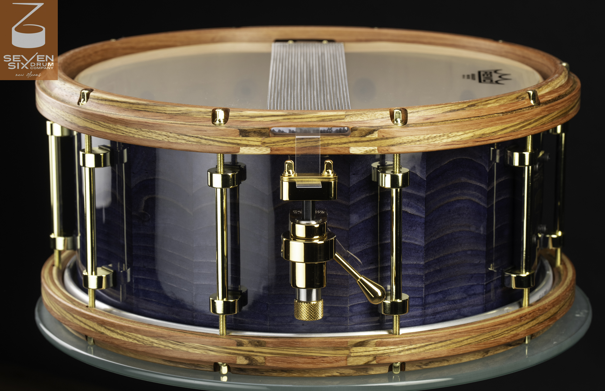 Handmade snare drum with a gloss blue-stained wood shell, natural wooden hoops, and polished gold hardware.