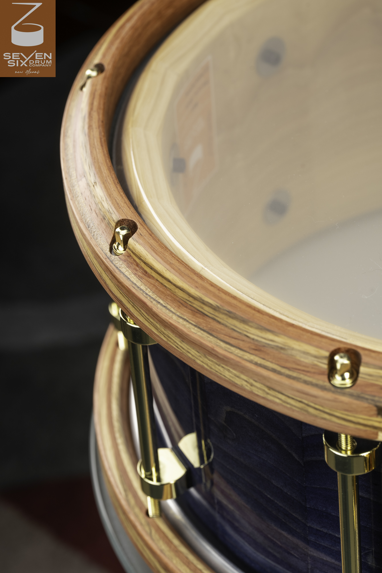 Handmade snare drum with a blue-stained wood shell, striped wooden hoops, and polished brass tube lugs.