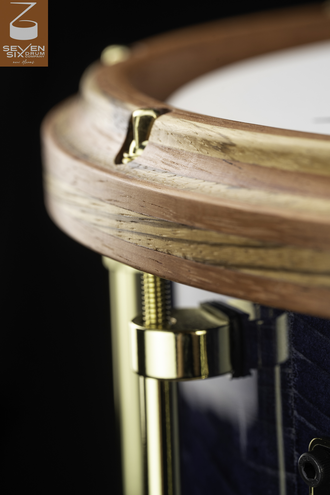 Handcrafted snare drum with a natural wood hoop, polished brass tension rod and lug, and a textured blue shell.