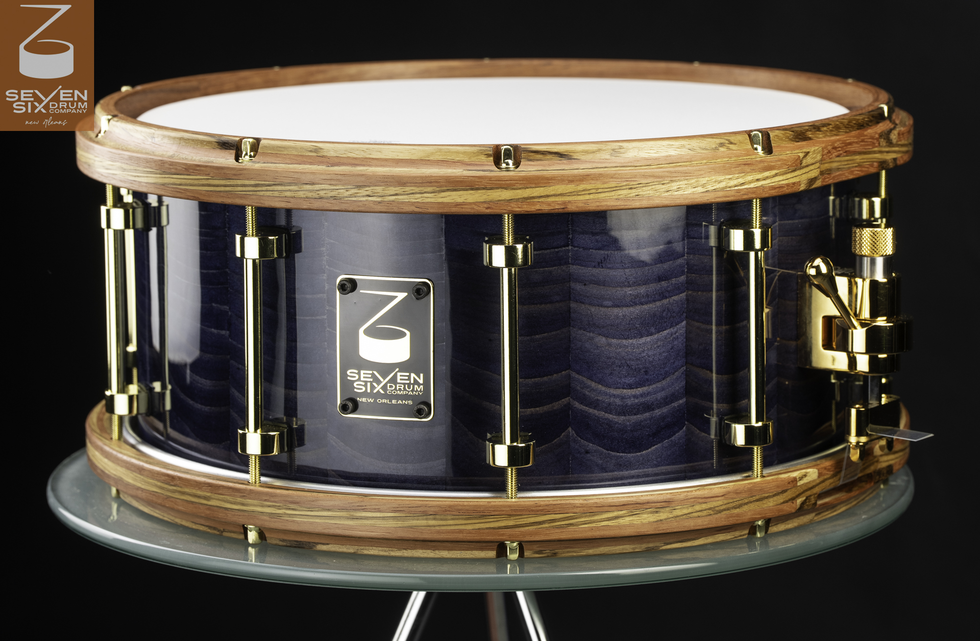 Handmade snare drum with a glossy blue figured wood shell, natural wooden hoops, and polished brass tube lugs.
