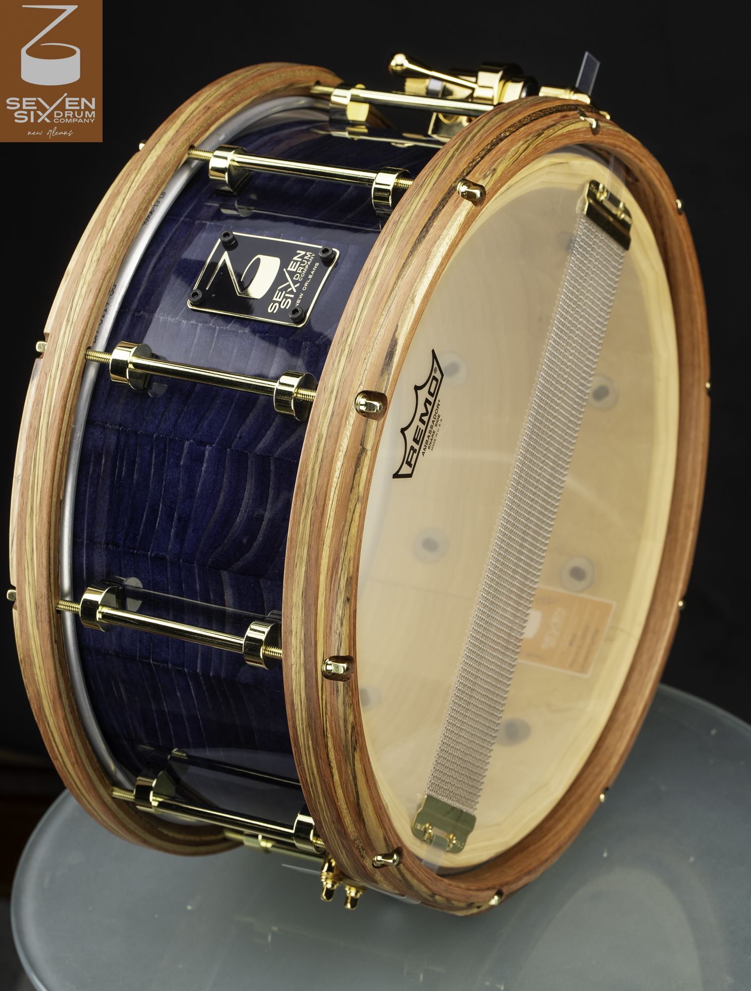 Handmade snare drum featuring a gloss blue figured wood shell, natural wood hoops, and polished gold hardware.