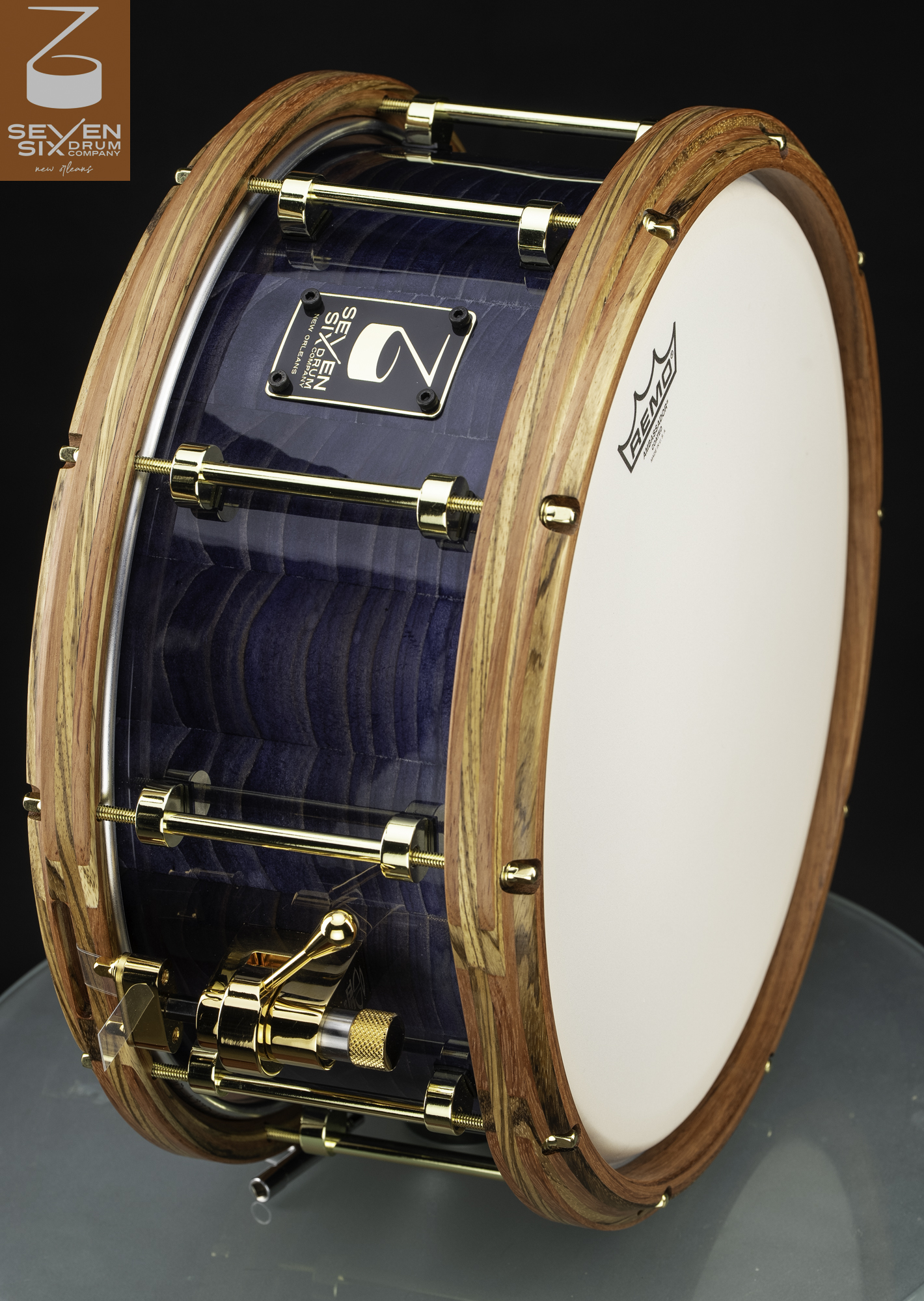 Handmade snare drum featuring a glossy blue figured wood shell, natural wood hoops, and gold hardware.