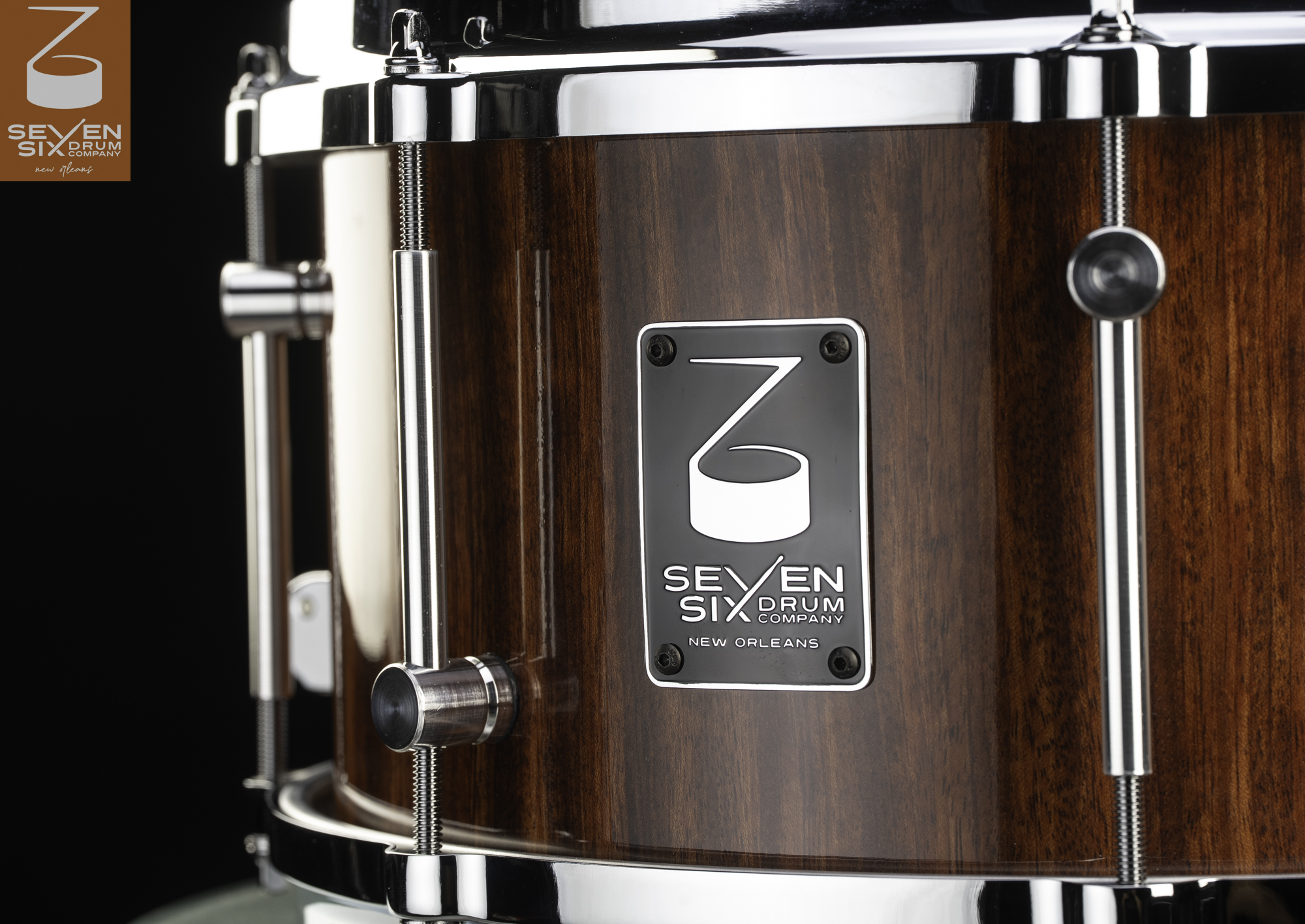 Handmade snare drum with a glossy brown wood shell, polished chrome tube lugs, and a black metal maker's badge.