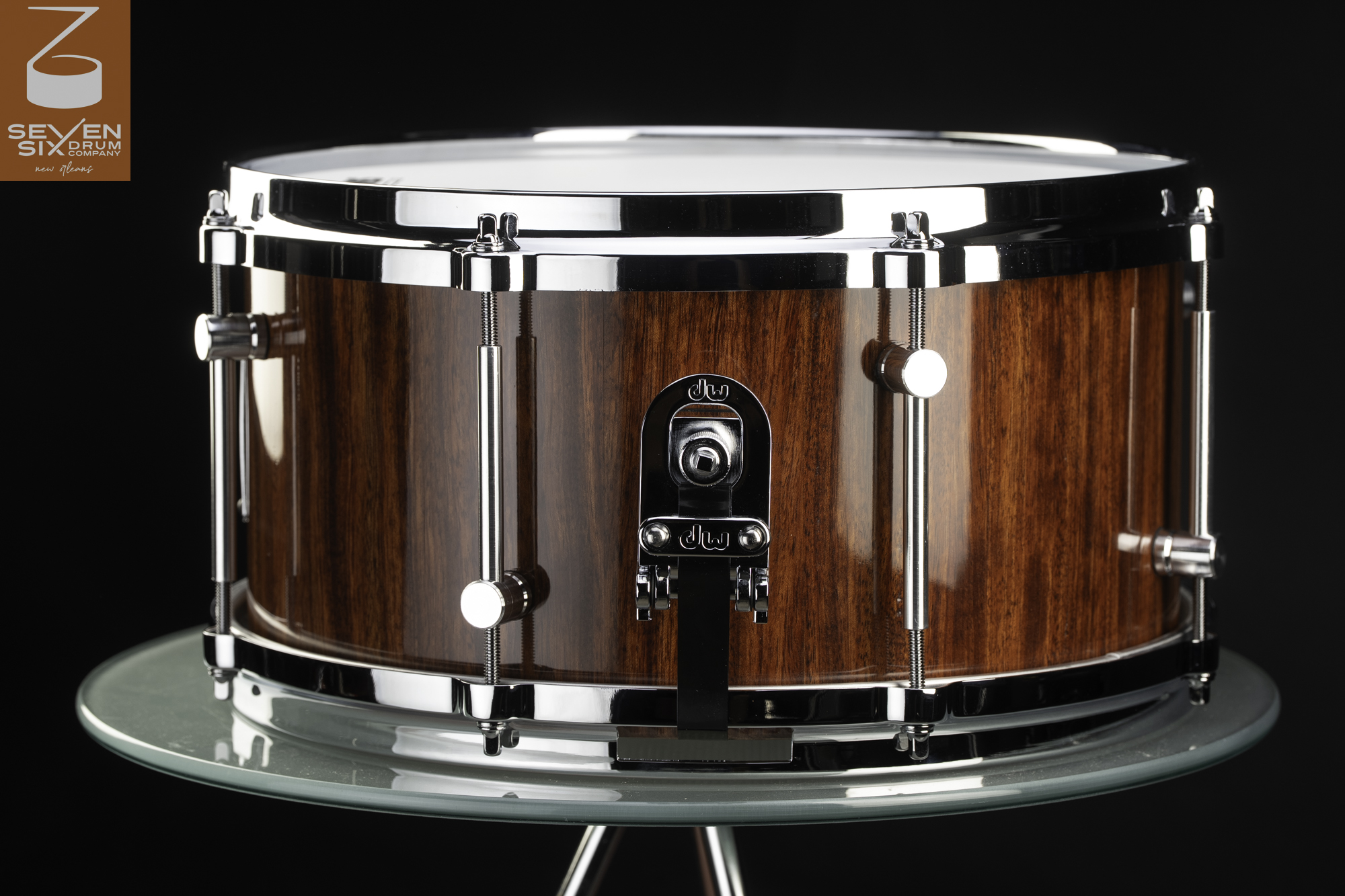 Handmade snare drum featuring a glossy reddish-brown wood shell, polished chrome hoops, tube lugs, and a DW throw-off.