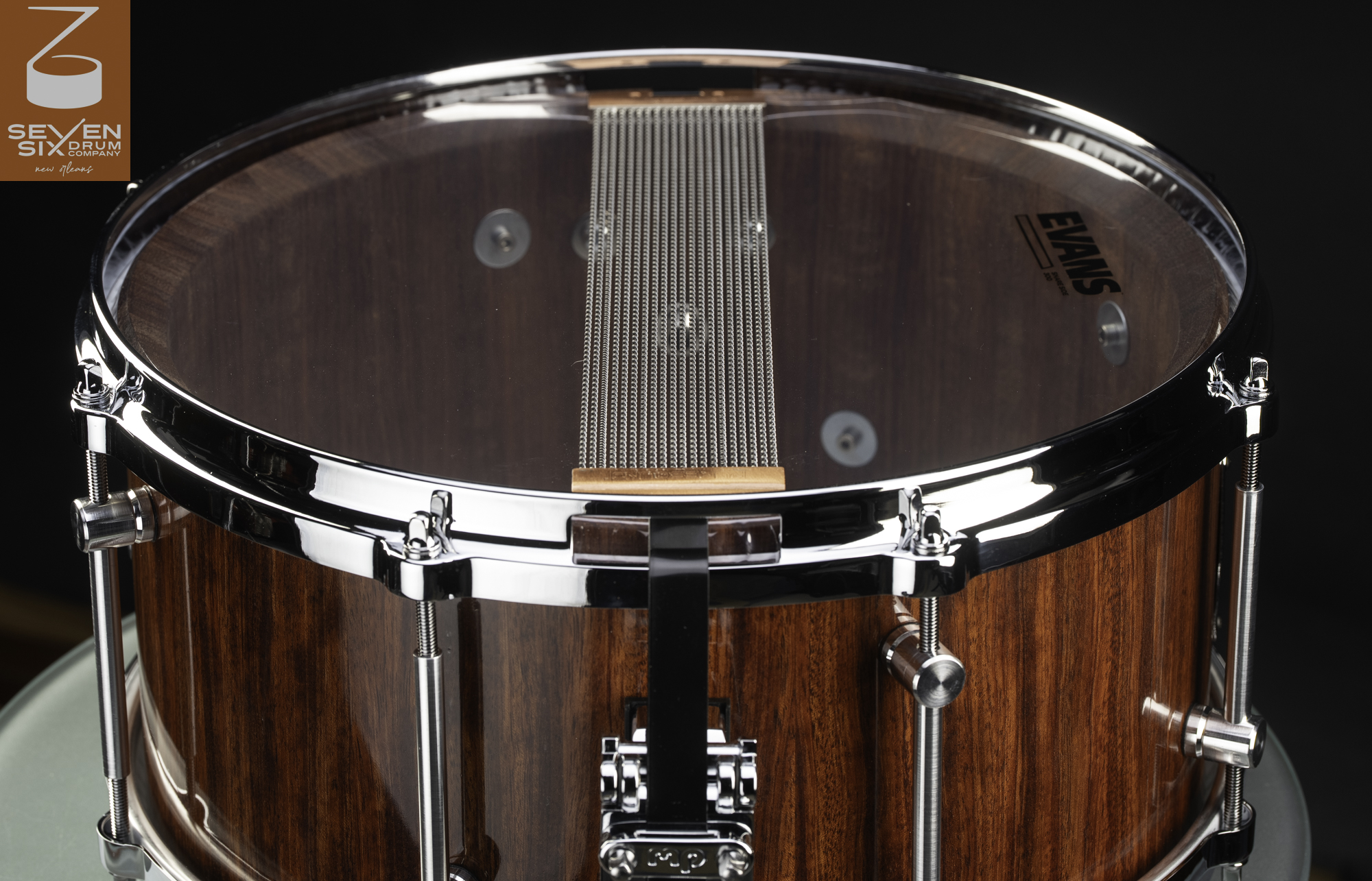 Handmade snare drum with a glossy natural wood shell, chrome hoops and lugs, and metal snare wires over a clear bottom head.