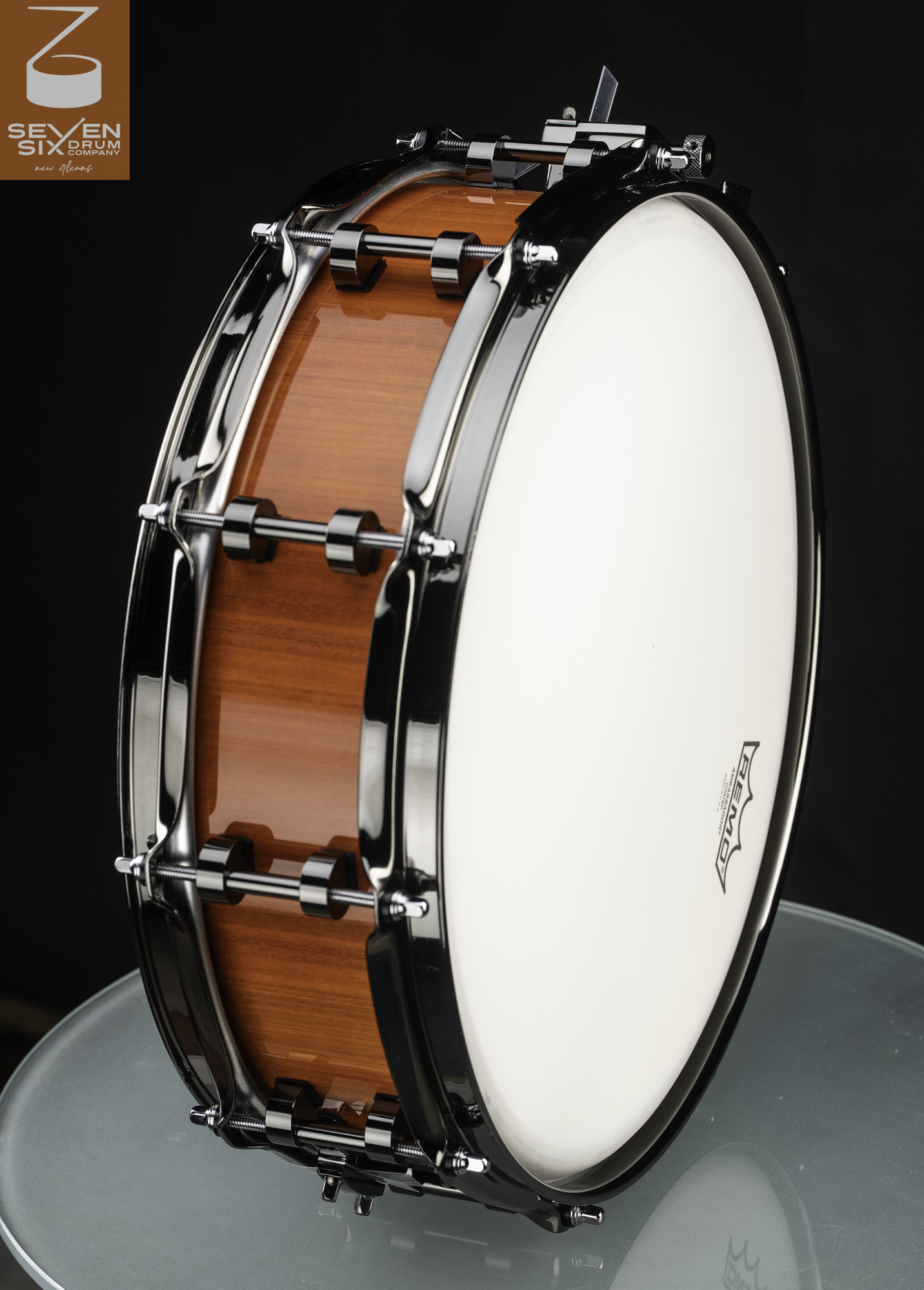 Handmade snare drum featuring a glossy amber wood shell, black nickel hardware, and a coated white Remo drumhead.