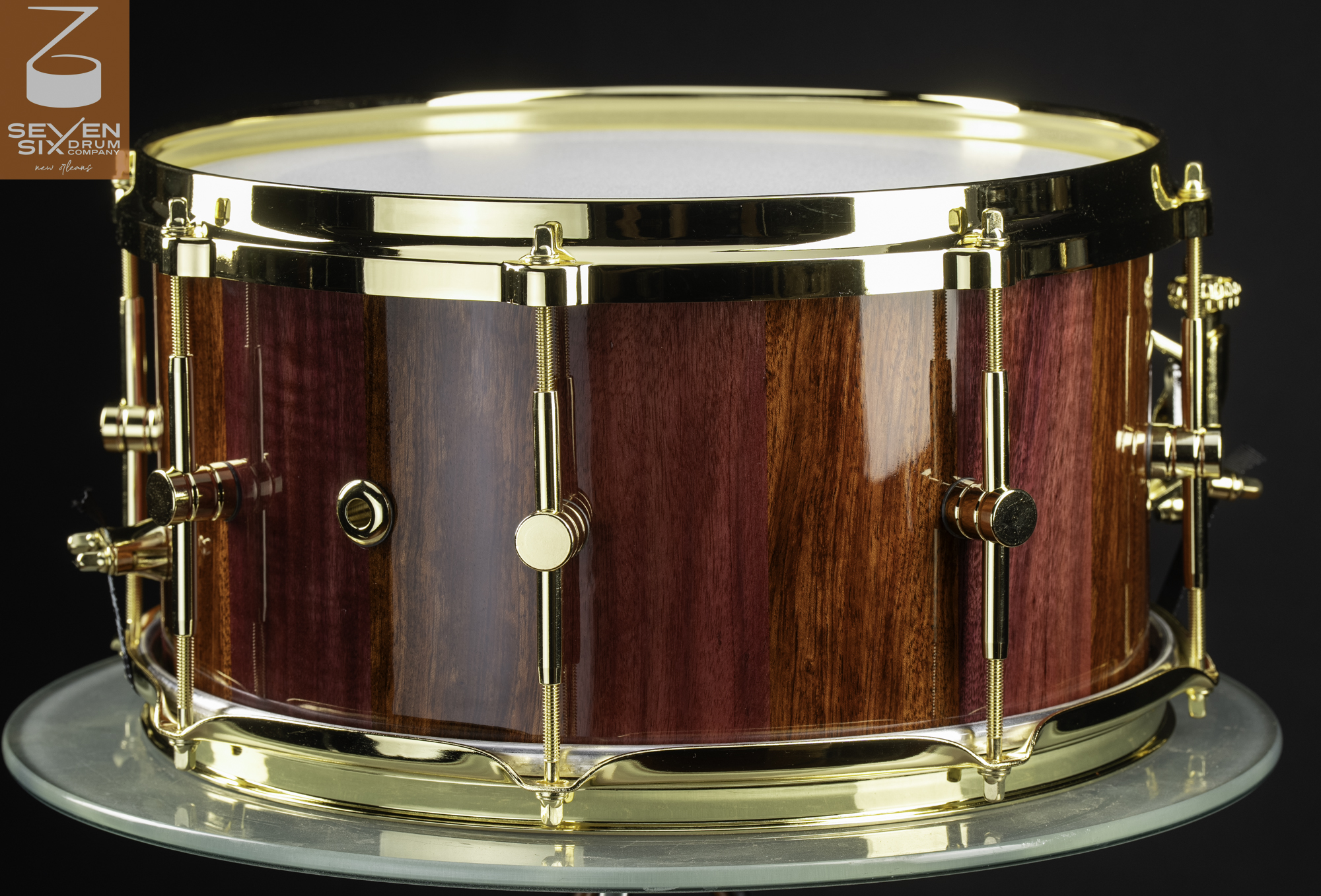 Handcrafted snare drum with a high-gloss striped purple and brown wood shell and polished gold hardware.