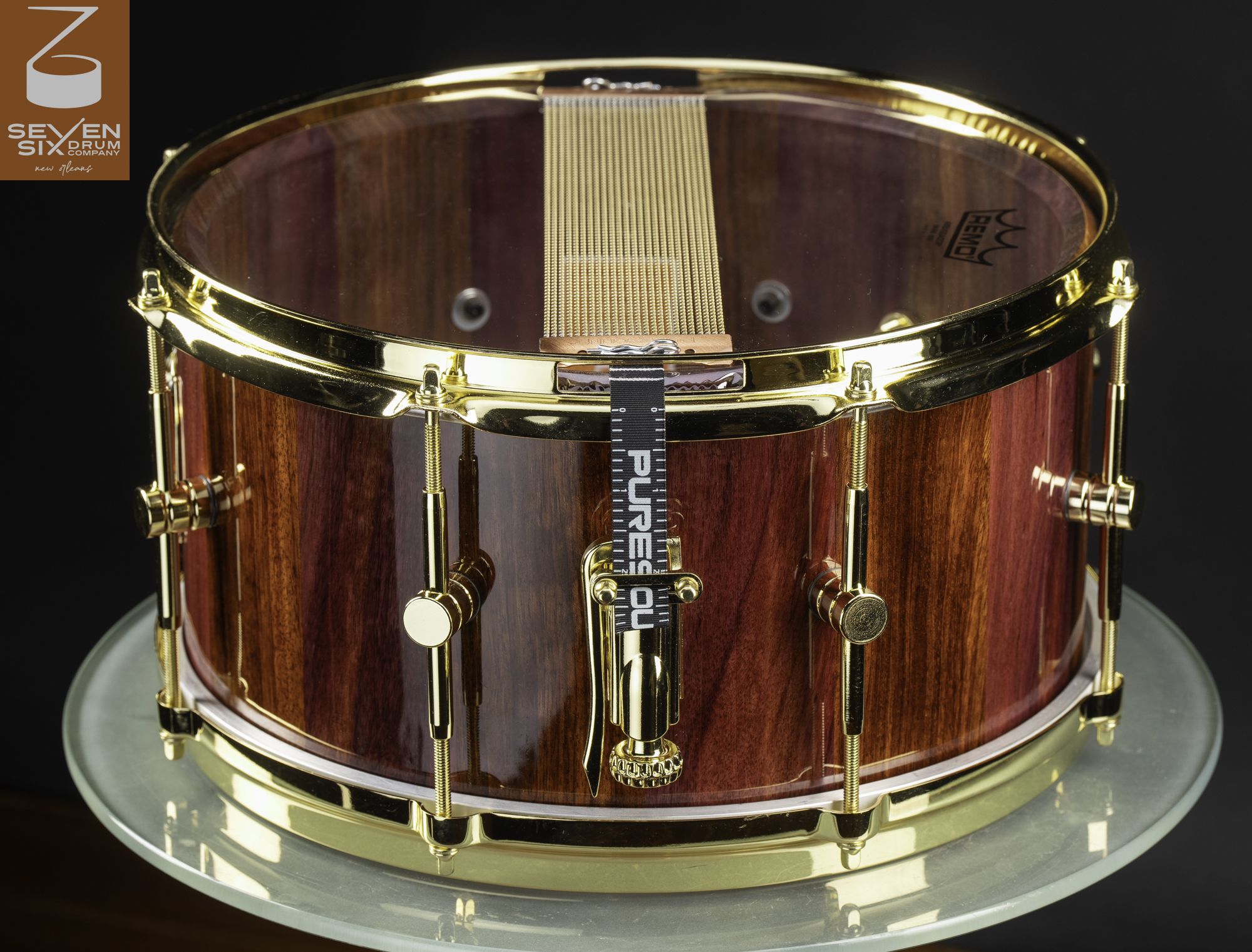 Handmade snare drum crafted from glossy striped red wood with polished gold hardware and snare wires.