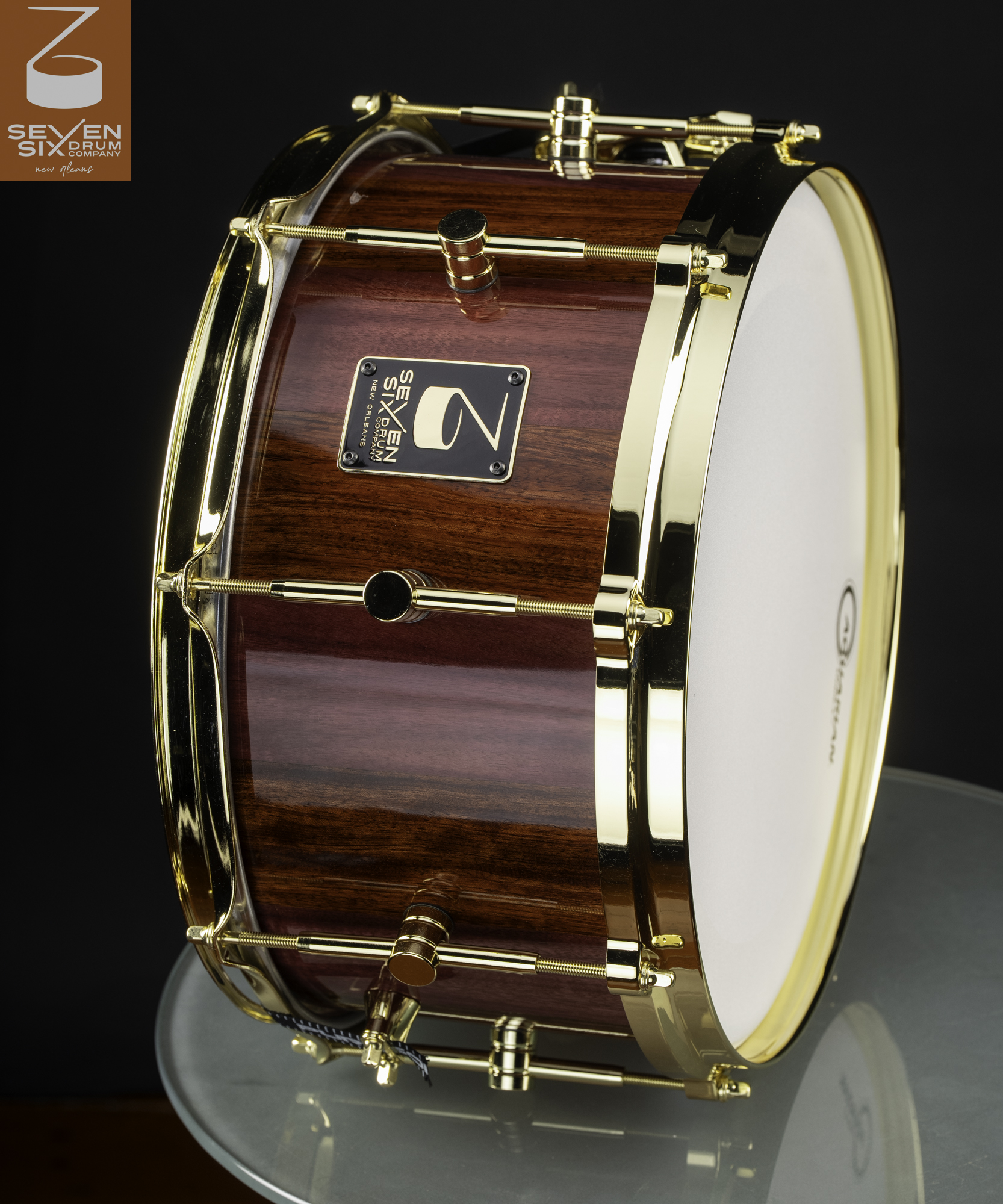Handcrafted snare drum with a glossy reddish-brown wood shell, polished gold hoops, and gold center lugs.