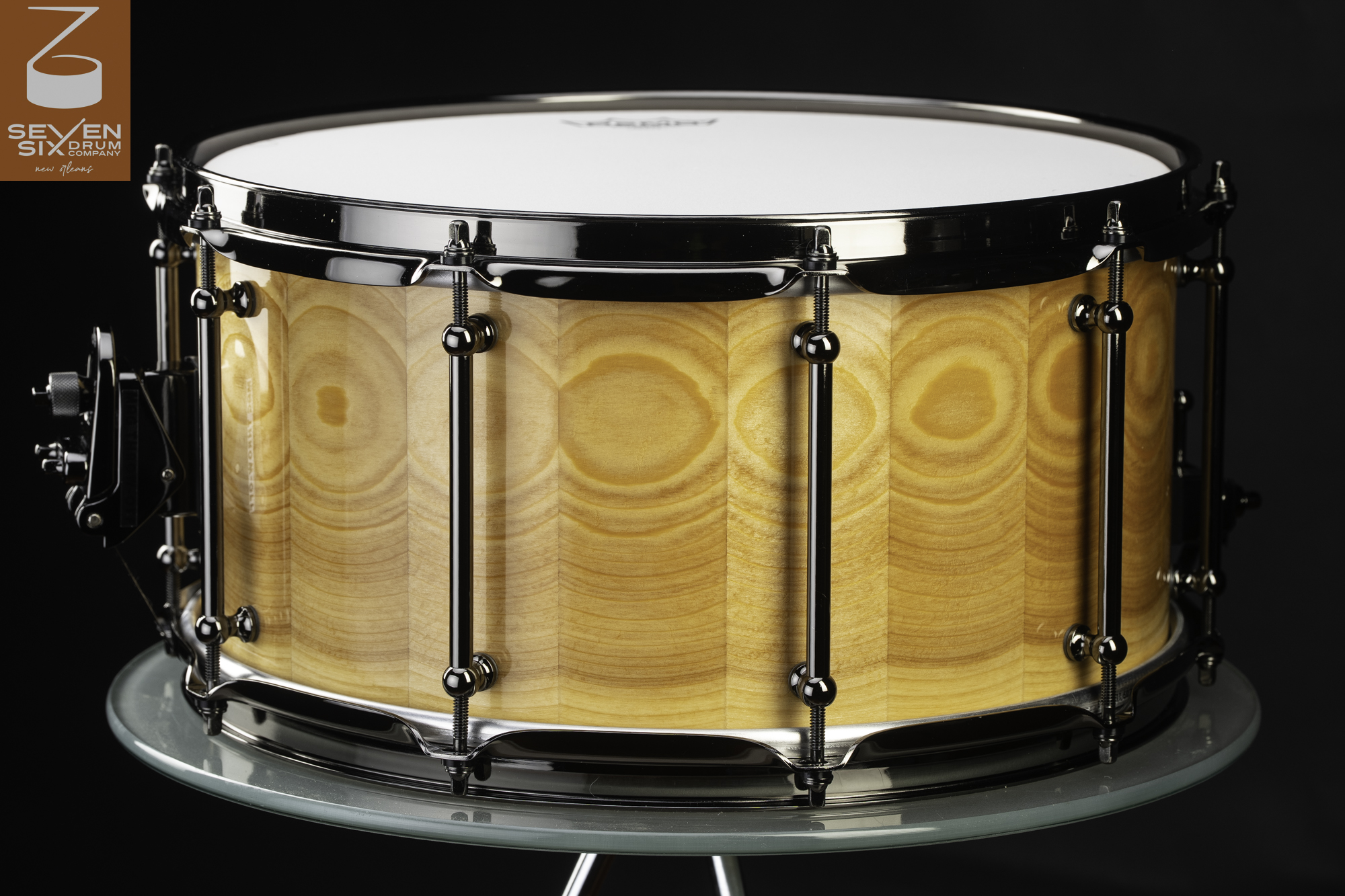 Handmade snare drum featuring a glossy natural stave wood shell with black nickel tube lugs and hoops.