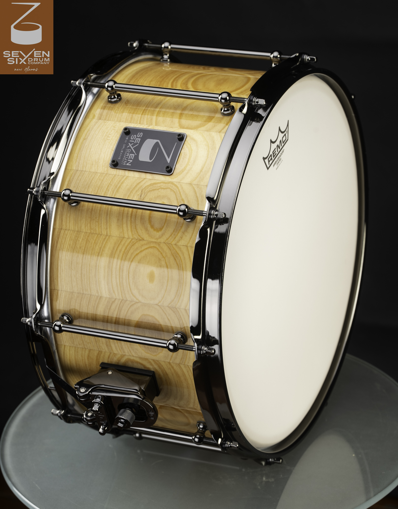 Glossy natural wood snare drum featuring black nickel tube lugs, matching hoops, and a snare throw-off.