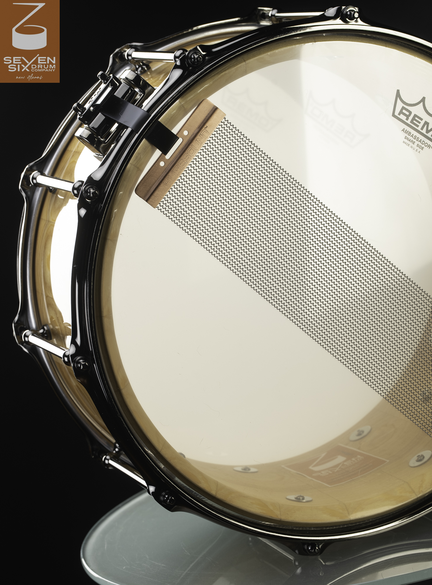 Underside of a natural gloss wood snare drum featuring chrome tube lugs, black flanged hoops, and wide snare wires.