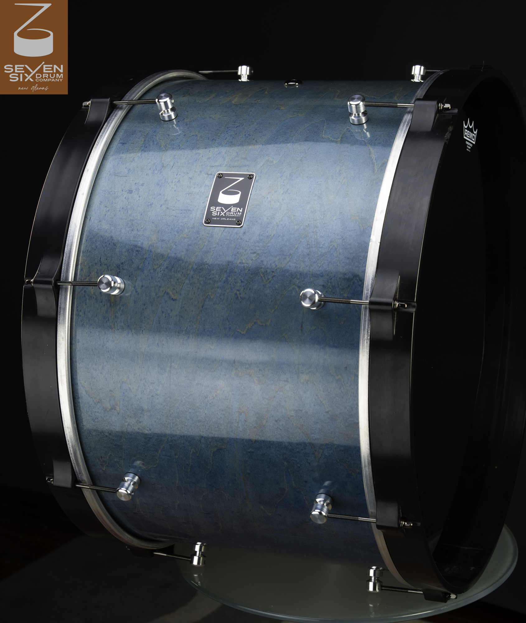 Handmade bass drum with a glossy teal wood grain finish, chrome lugs, and black wooden hoops.