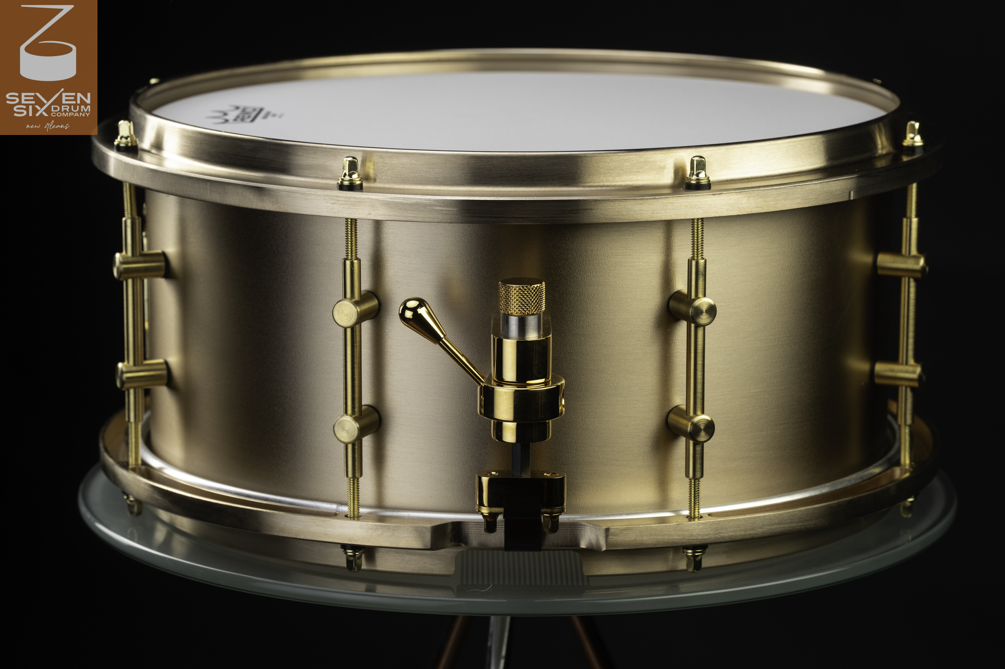 Brushed brass snare drum with matching metal hoops, brass tube lugs, and a polished gold throw-off.