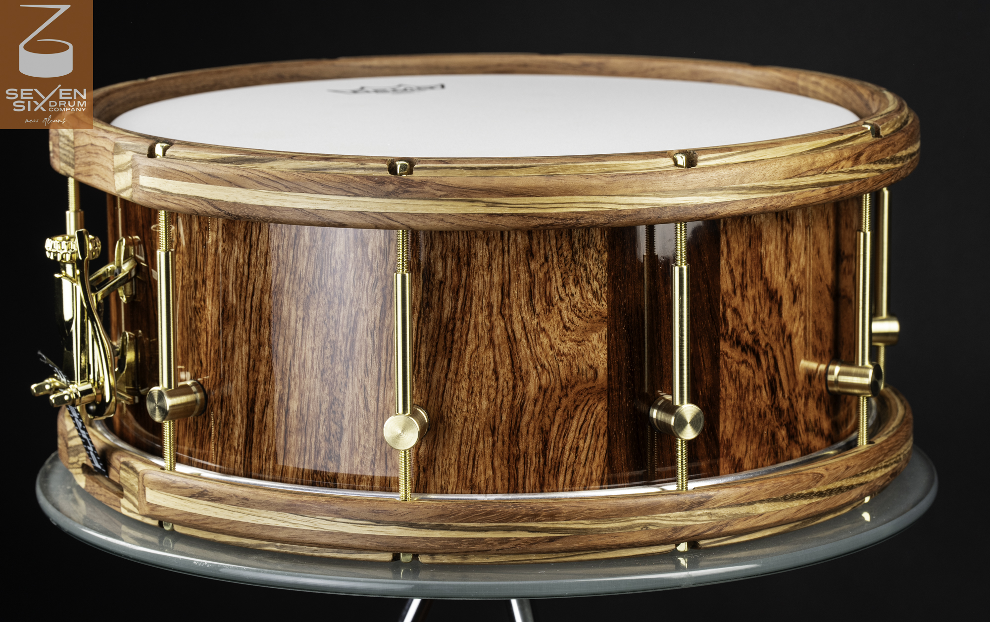 Handmade snare drum with a glossy figured wood shell, matching wooden hoops, and brass hardware.
