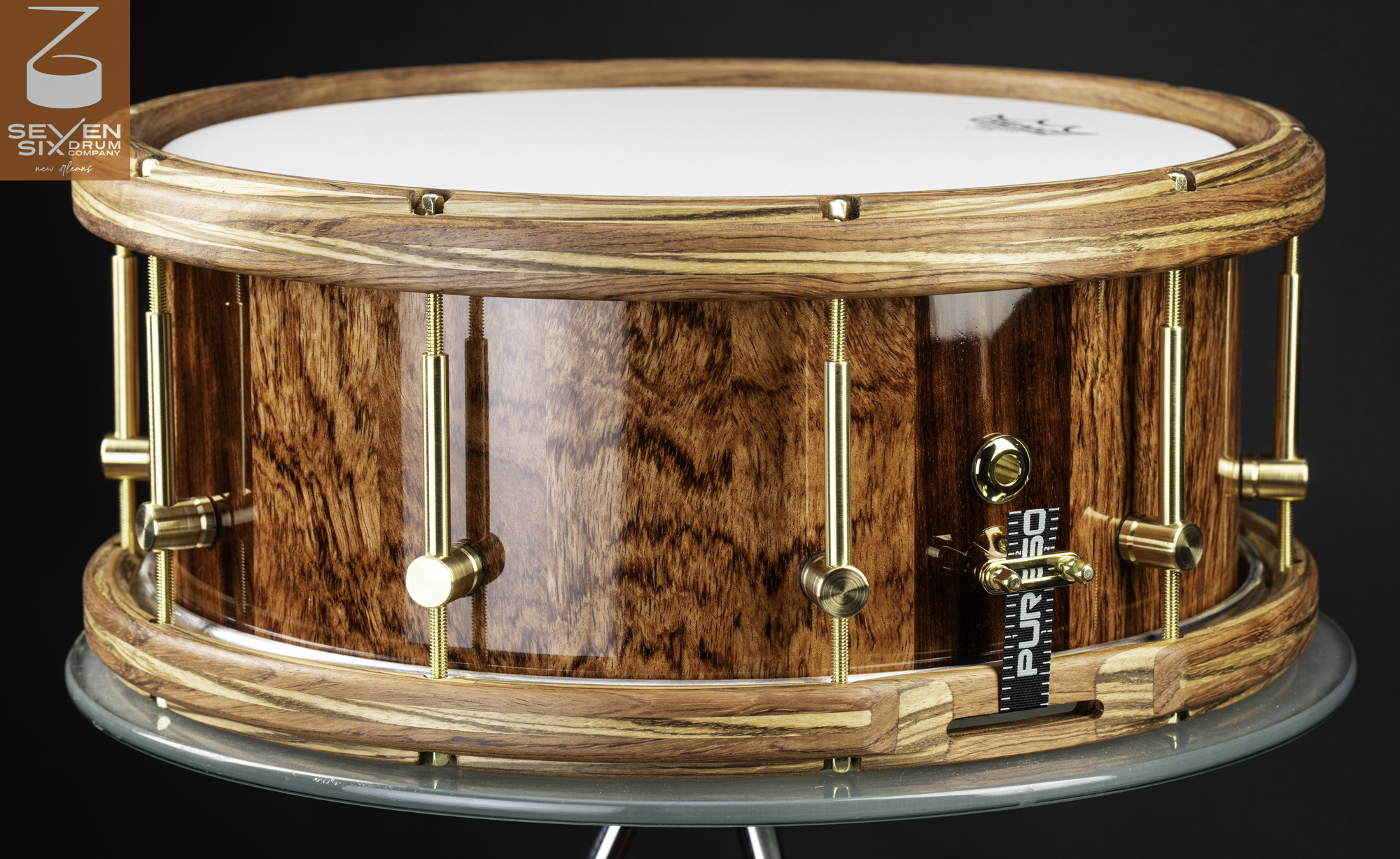 Handmade snare drum with a glossy wood shell, laminated wooden hoops, and brushed brass hardware.