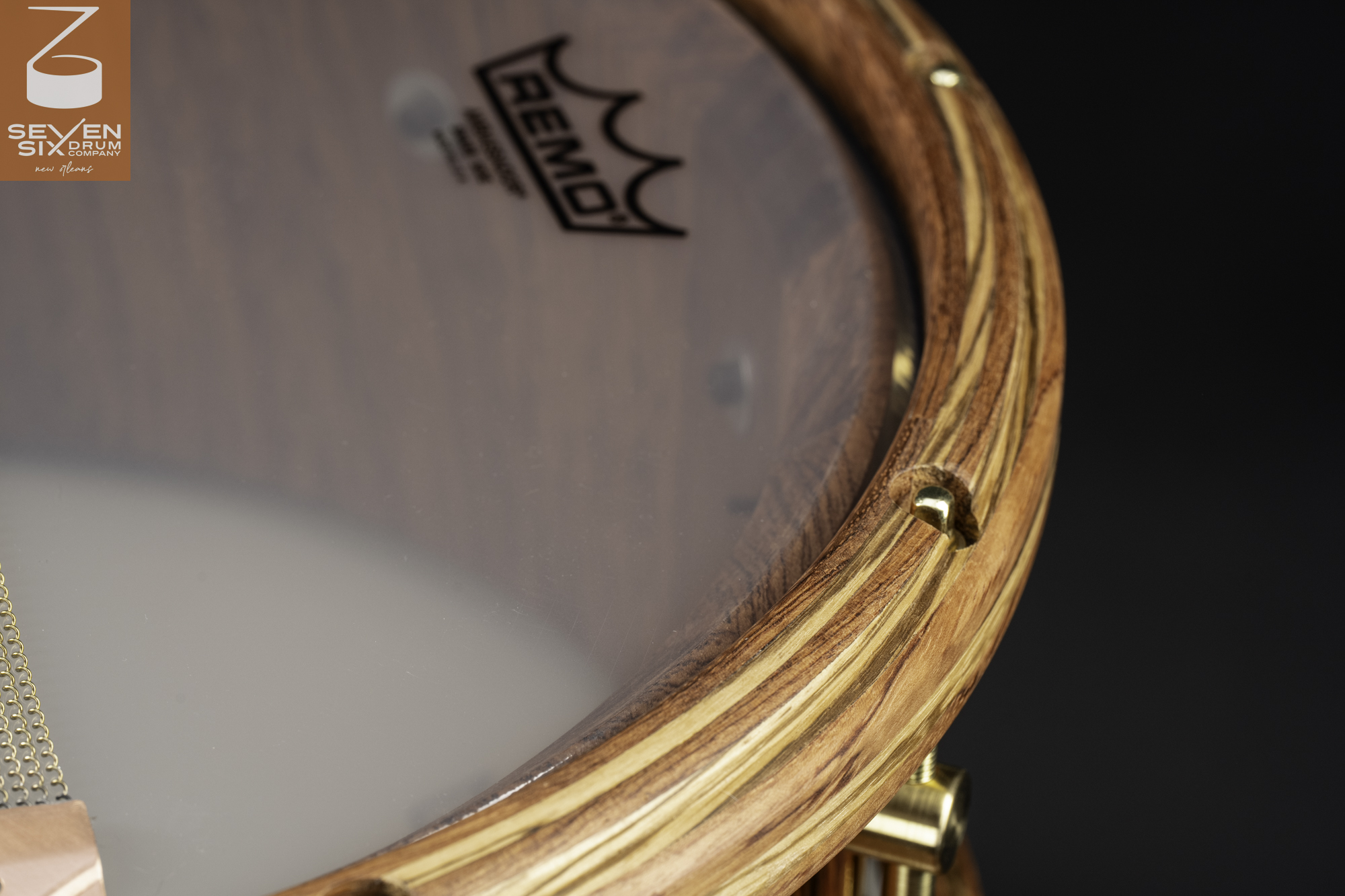 Handmade snare drum with a natural striped wood hoop, brass hardware, and snare wires over a clear Remo head.