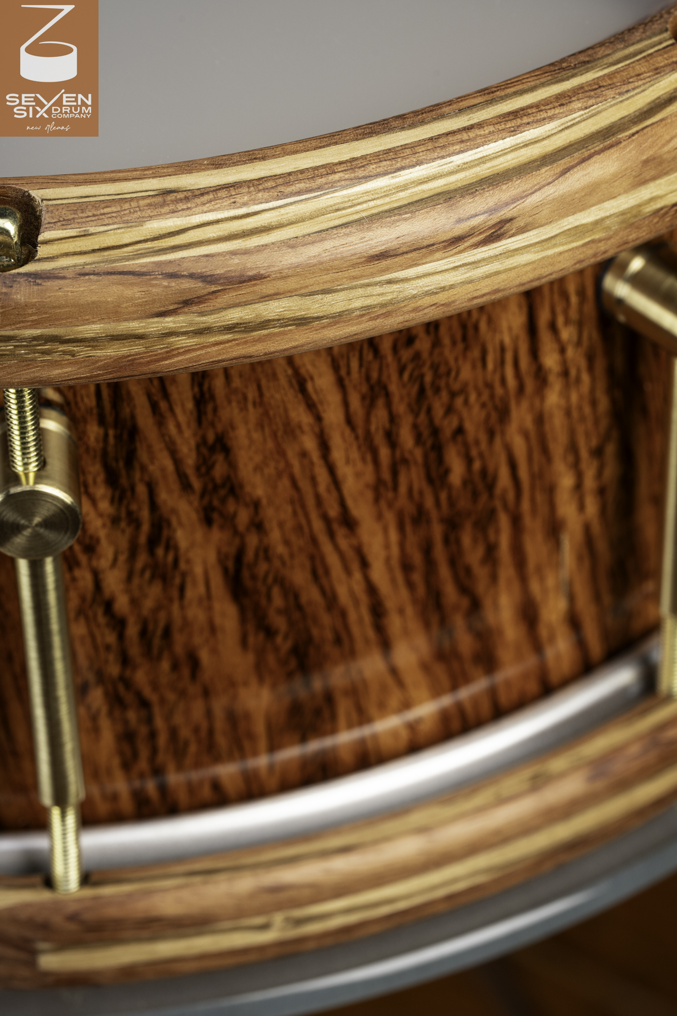 Glossy figured wood snare drum featuring layered wooden hoops and brushed brass hardware.