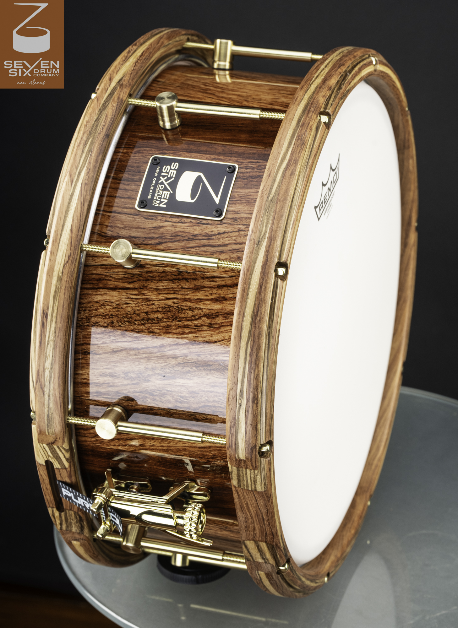 Handmade wood snare drum with a high-gloss finish, segmented wood hoops, and polished brass hardware.