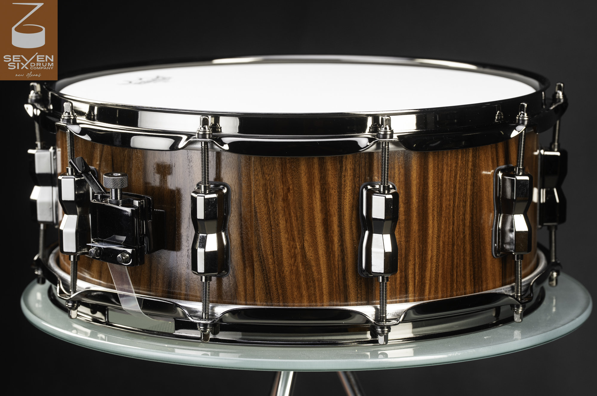 Handmade snare drum featuring a glossy vertical-grain wood shell, black nickel hoops, lugs, and throw-off.