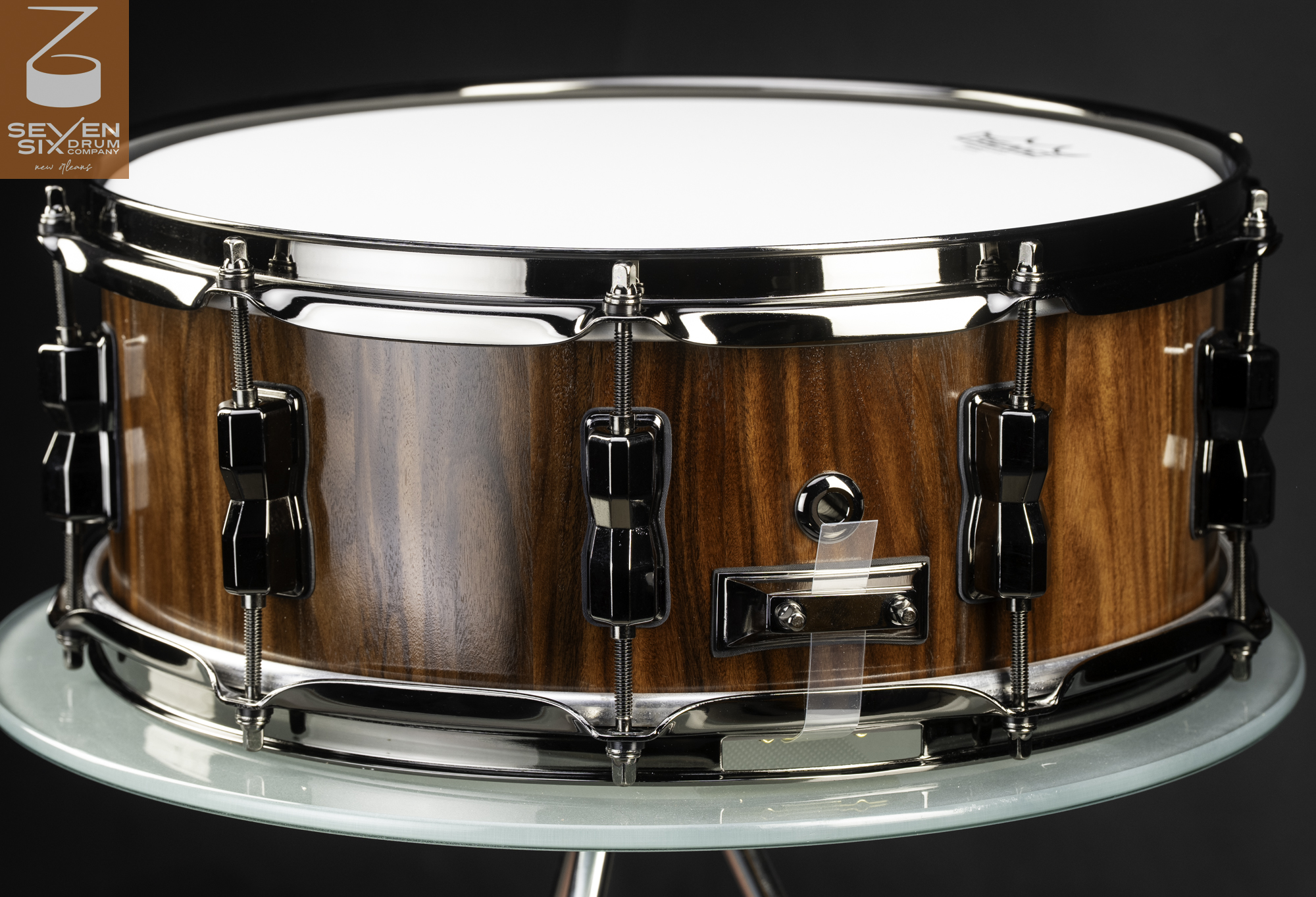 Handcrafted snare drum featuring a glossy natural wood shell with black nickel hoops, lugs, and butt plate.