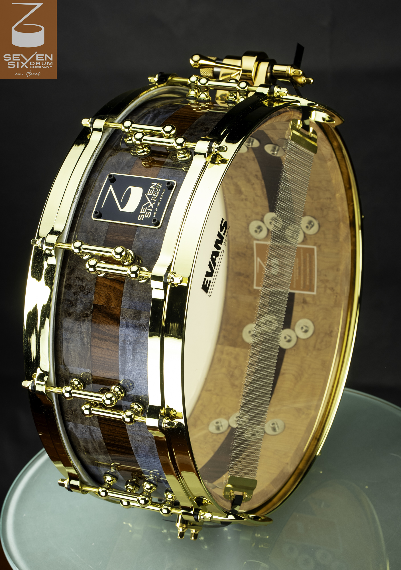 Handmade snare drum featuring a glossy segmented wood shell with polished gold hoops and tube lugs.