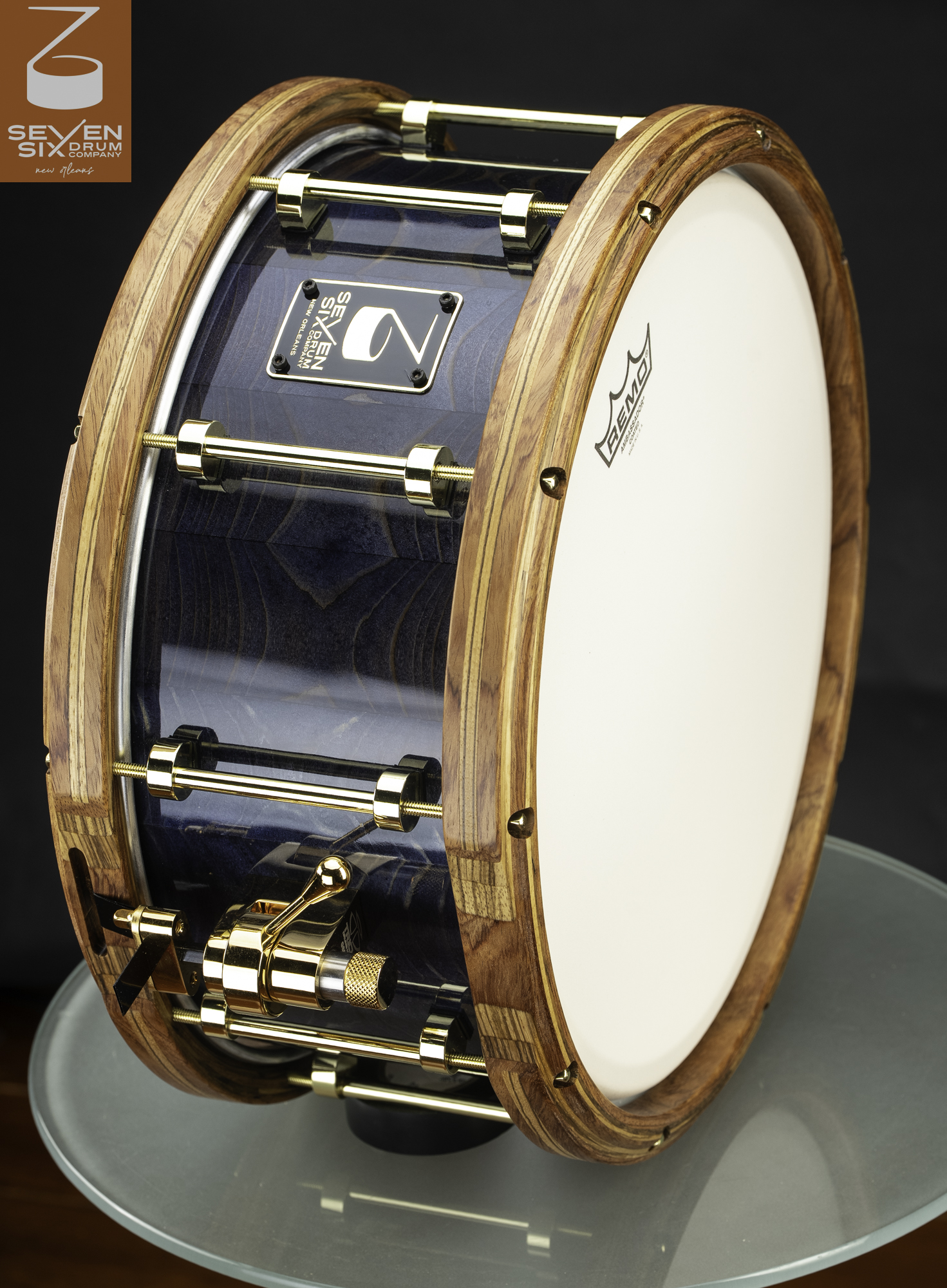 Handmade snare drum featuring a glossy blue wood shell, natural segmented wood hoops, and polished gold tube lugs.
