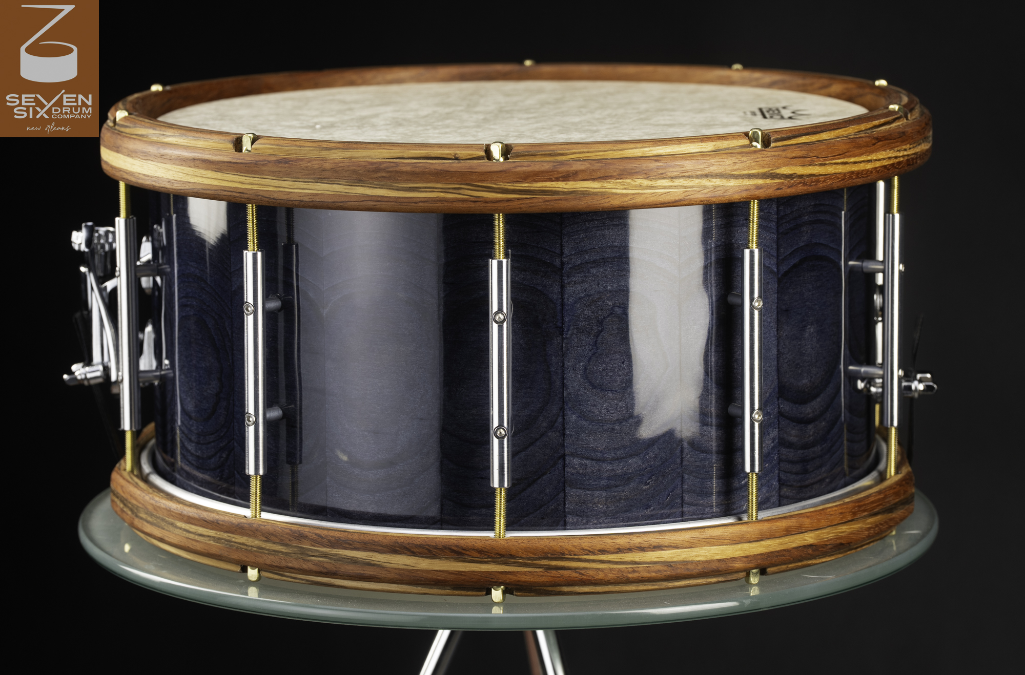 Handcrafted snare drum with a gloss blue wood shell, natural wood hoops, and chrome tube lugs with brass tension rods.