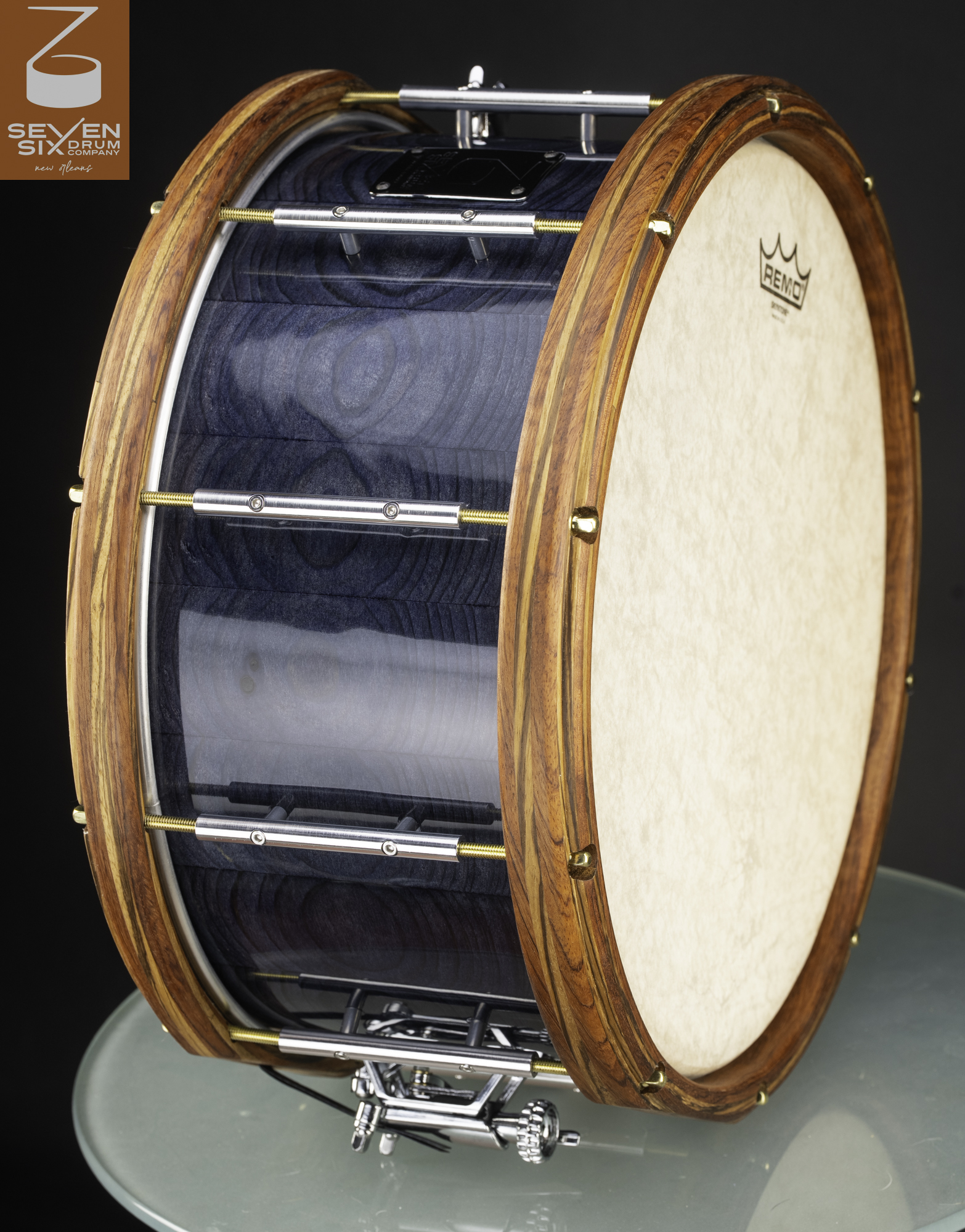 A handmade snare drum with a glossy blue wood shell, striped natural wood hoops, and chrome tube lugs with brass tension rods.