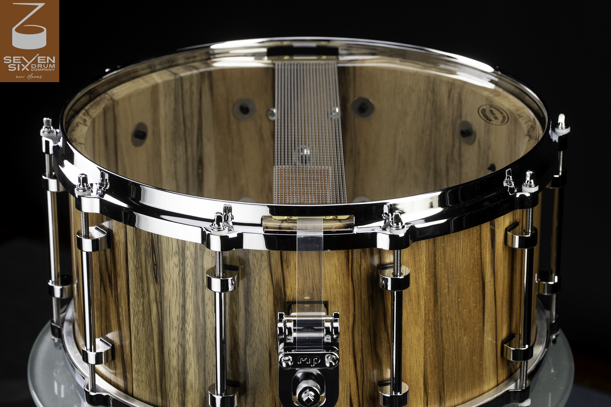 Handmade snare drum with a striped natural wood shell, chrome hardware, tube lugs, and snare wires over a clear resonant head.
