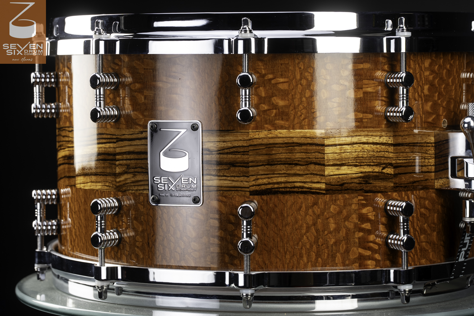 Handmade gloss wood snare drum with a central zebrawood band, chrome hoops, and double tube lugs.