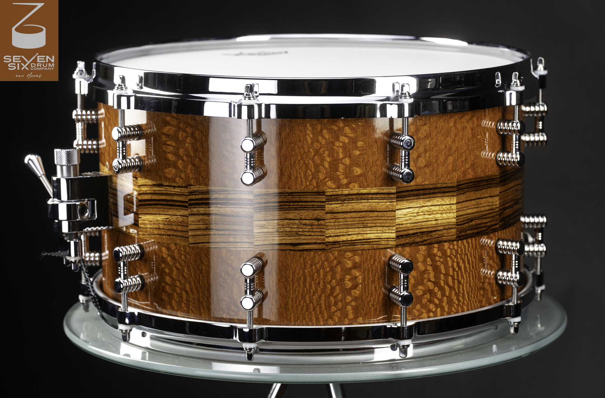 Handmade snare drum with a high-gloss figured wood shell, zebrawood center band, and chrome hardware.