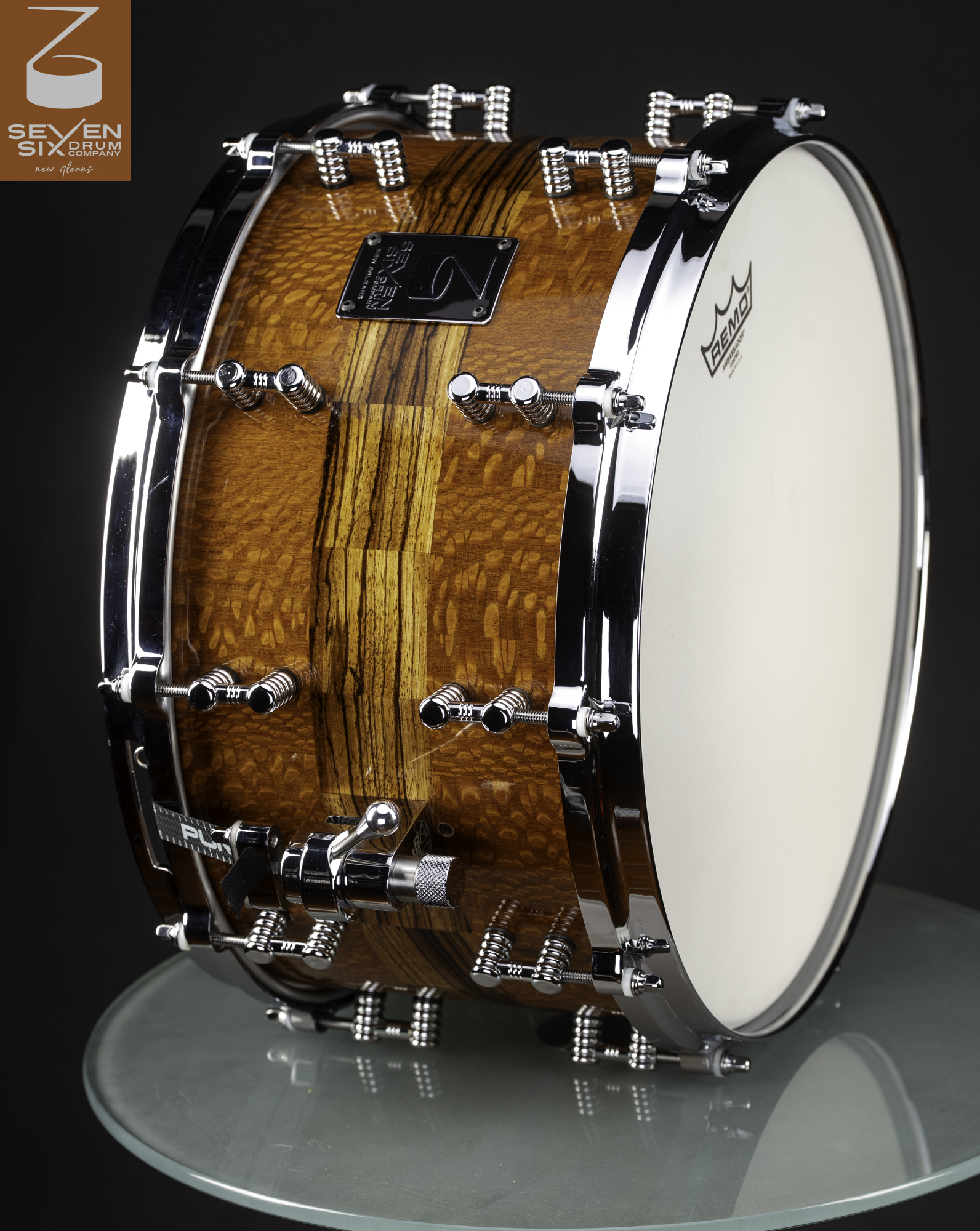 Handmade snare drum featuring a gloss segmented wood shell with polished chrome hoops, lugs, and a throw-off.