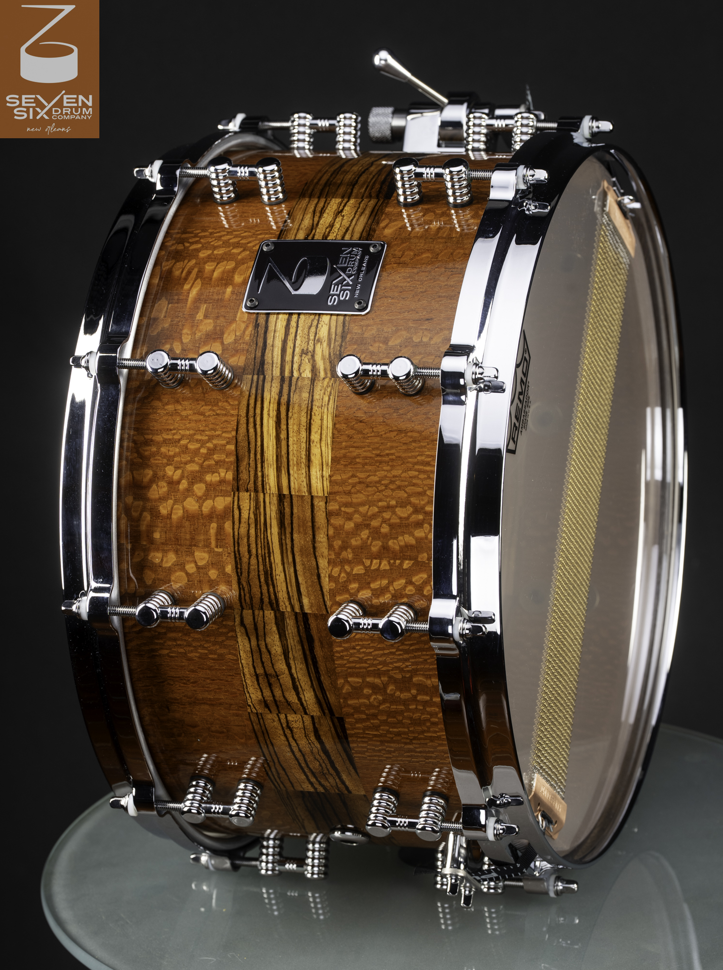 Handmade snare drum crafted in high-gloss figured wood with a zebrawood stripe, featuring polished chrome hoops and lugs.
