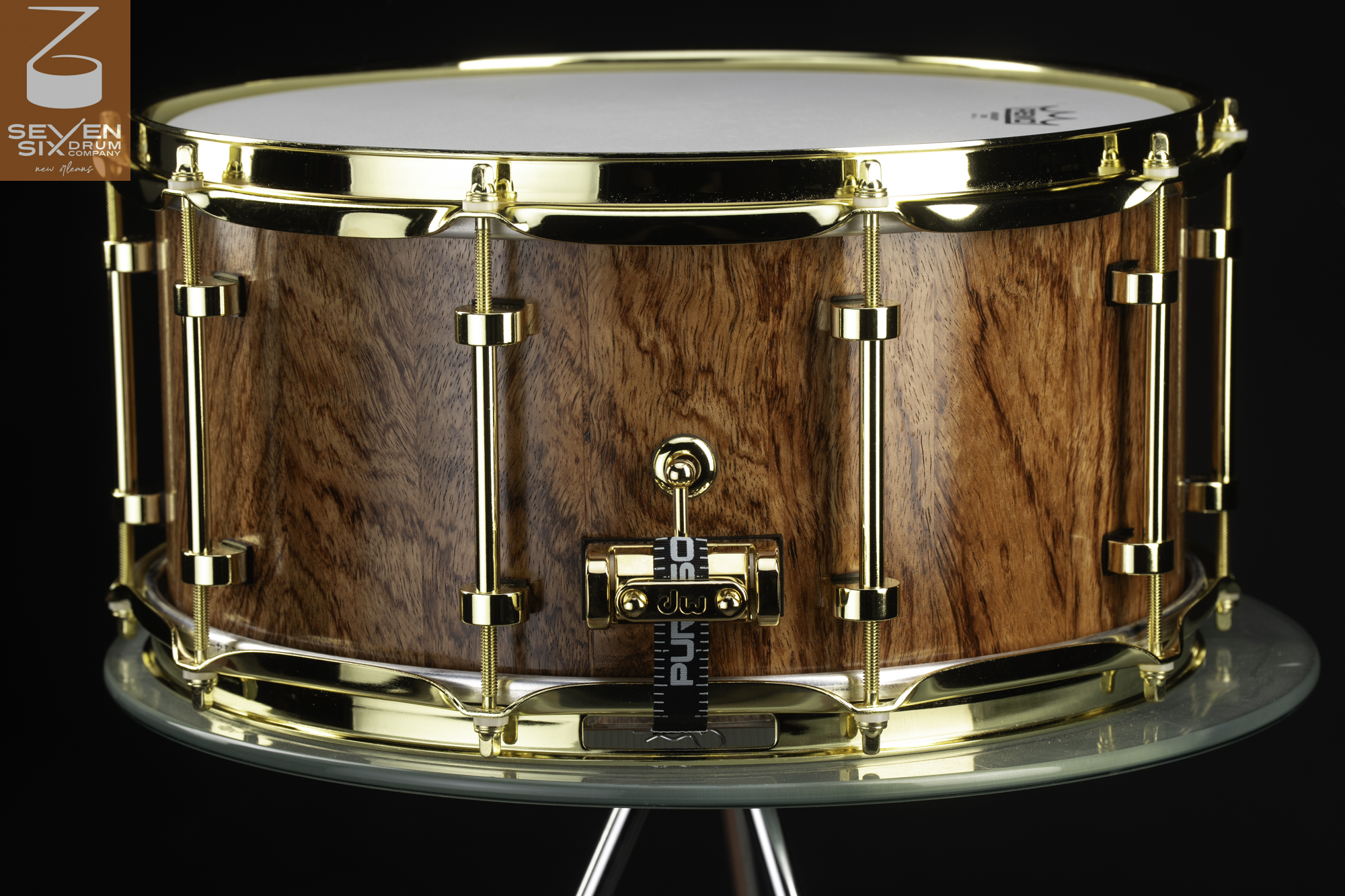 Wooden snare drum with a glossy natural grain shell, polished gold-plated hoops, and matching gold tube lugs.