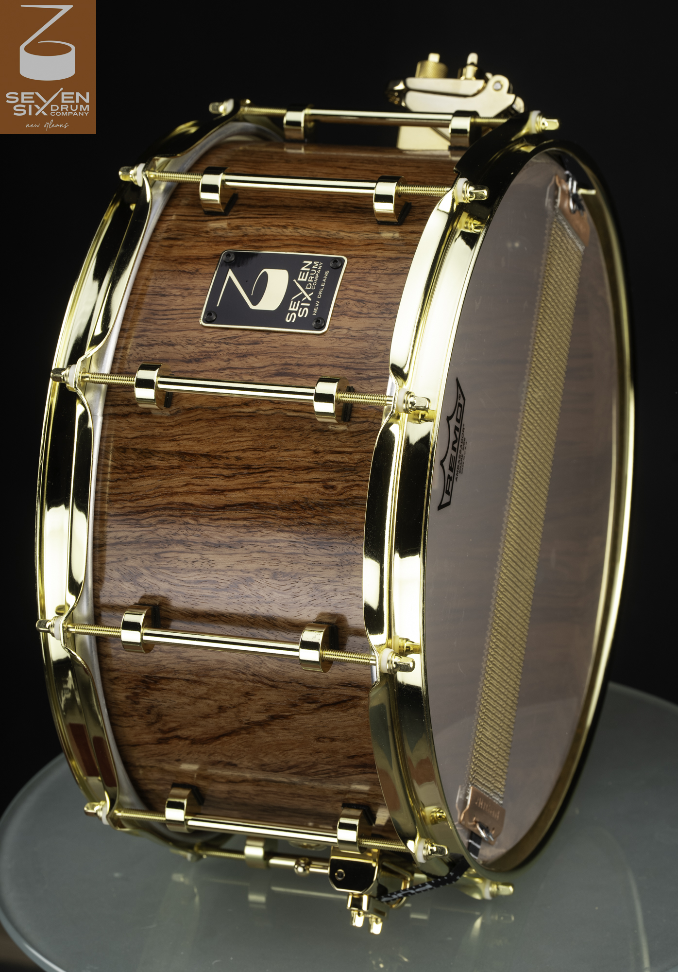 Handmade snare drum featuring a glossy natural wood shell with polished gold-plated hoops and tube lugs.