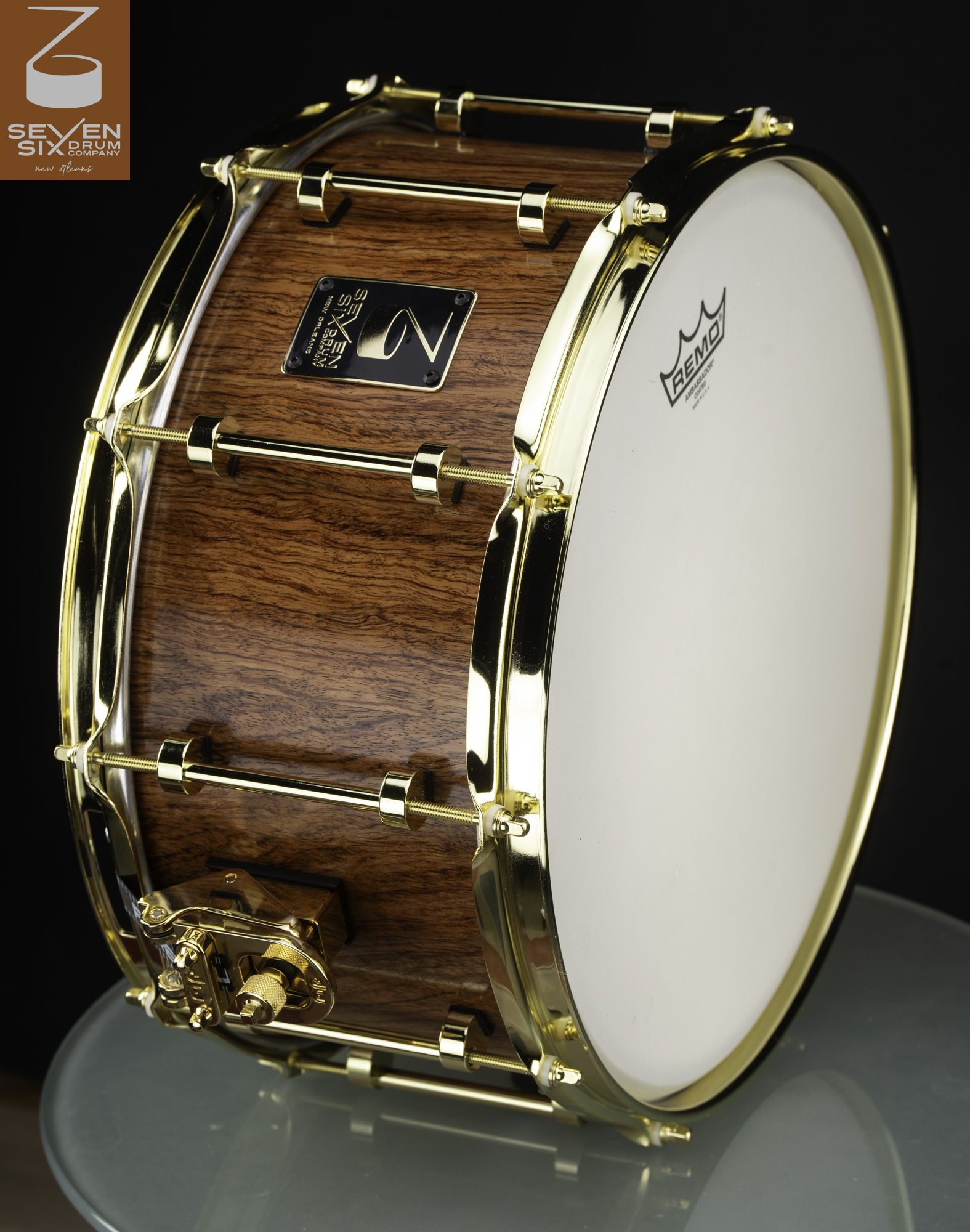 Handmade snare drum featuring a rich brown wood grain shell with polished gold hoops, tube lugs, and throw-off.
