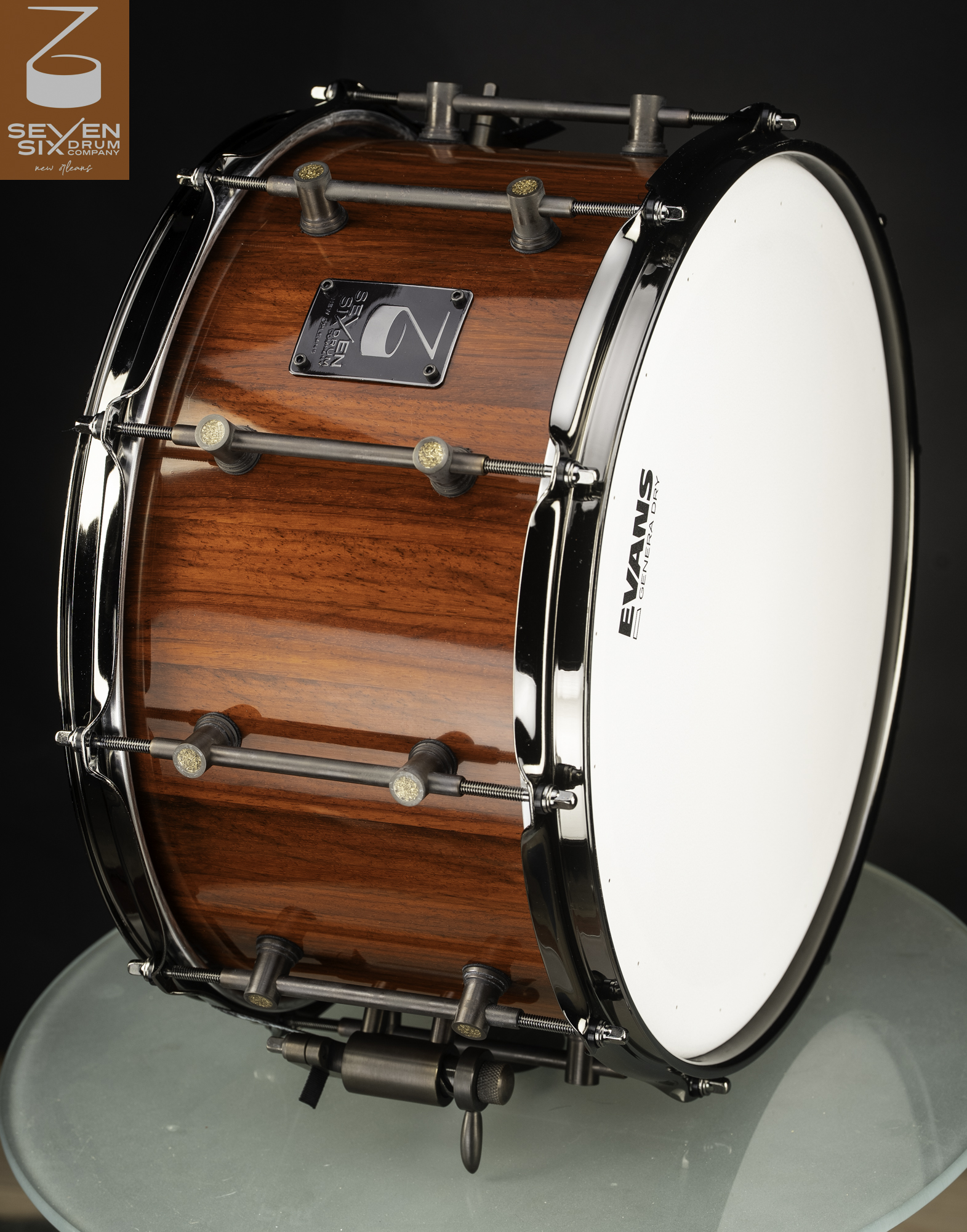 Deep wood snare drum with a glossy reddish-brown finish, black nickel hoops, and antique bronze tube lugs.