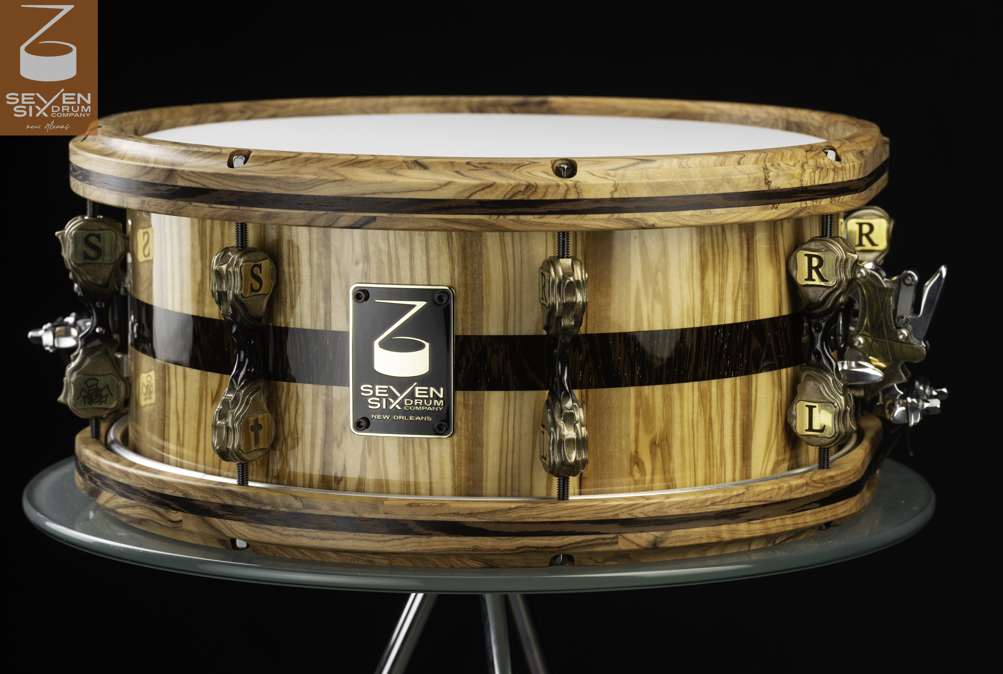 Handmade snare drum in gloss natural wood with a dark stripe, matching wooden hoops, and custom antique brass lugs.