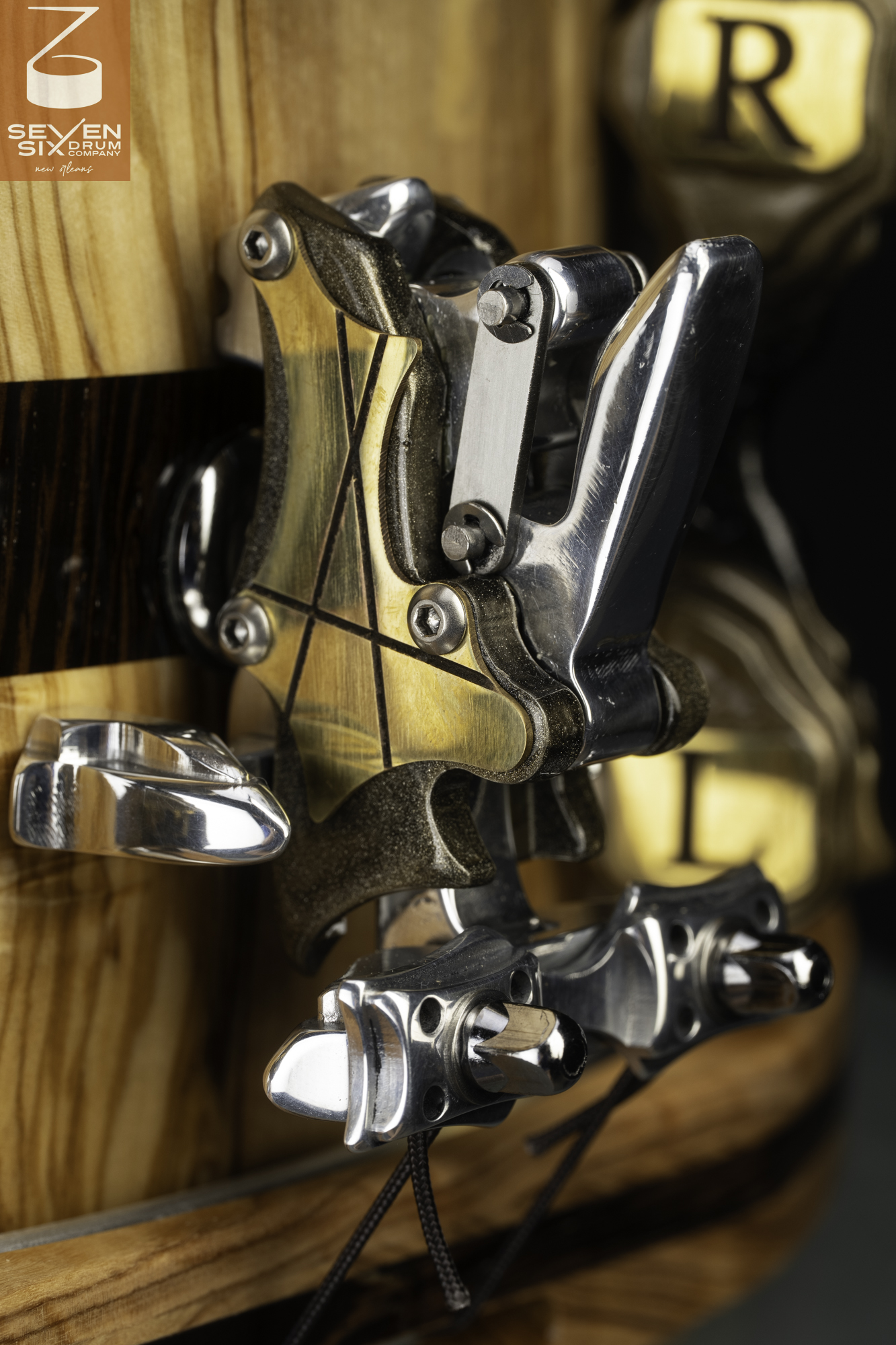 A custom brass and chrome snare throw-off mechanism mounted on a natural-finish wood drum shell.