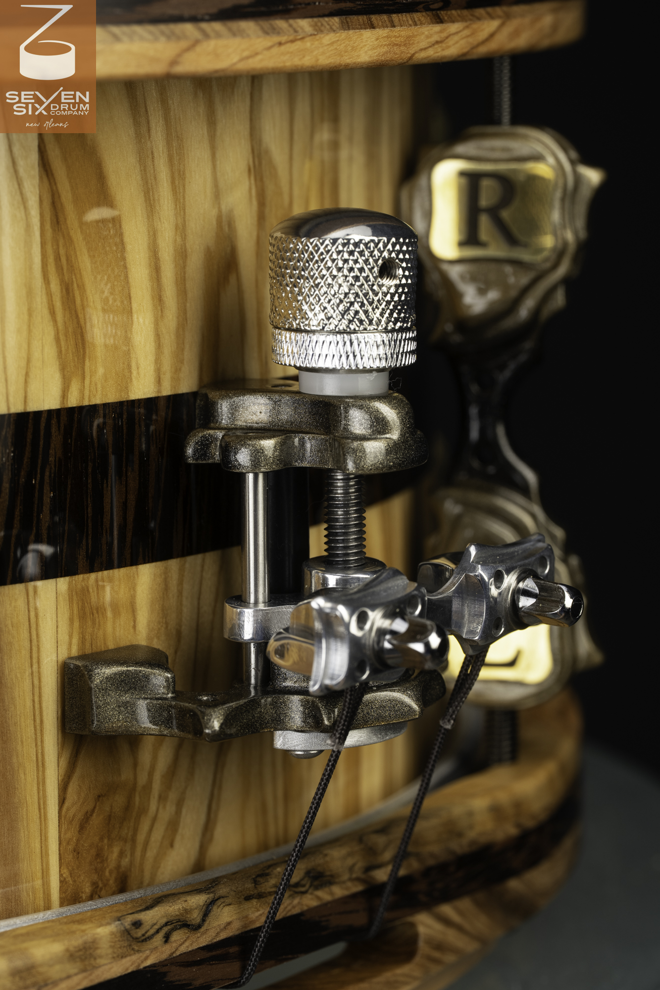 Close-up of a metal snare throw-off mounted on a glossy wood drum shell with a dark inlay stripe and matching wood hoops.