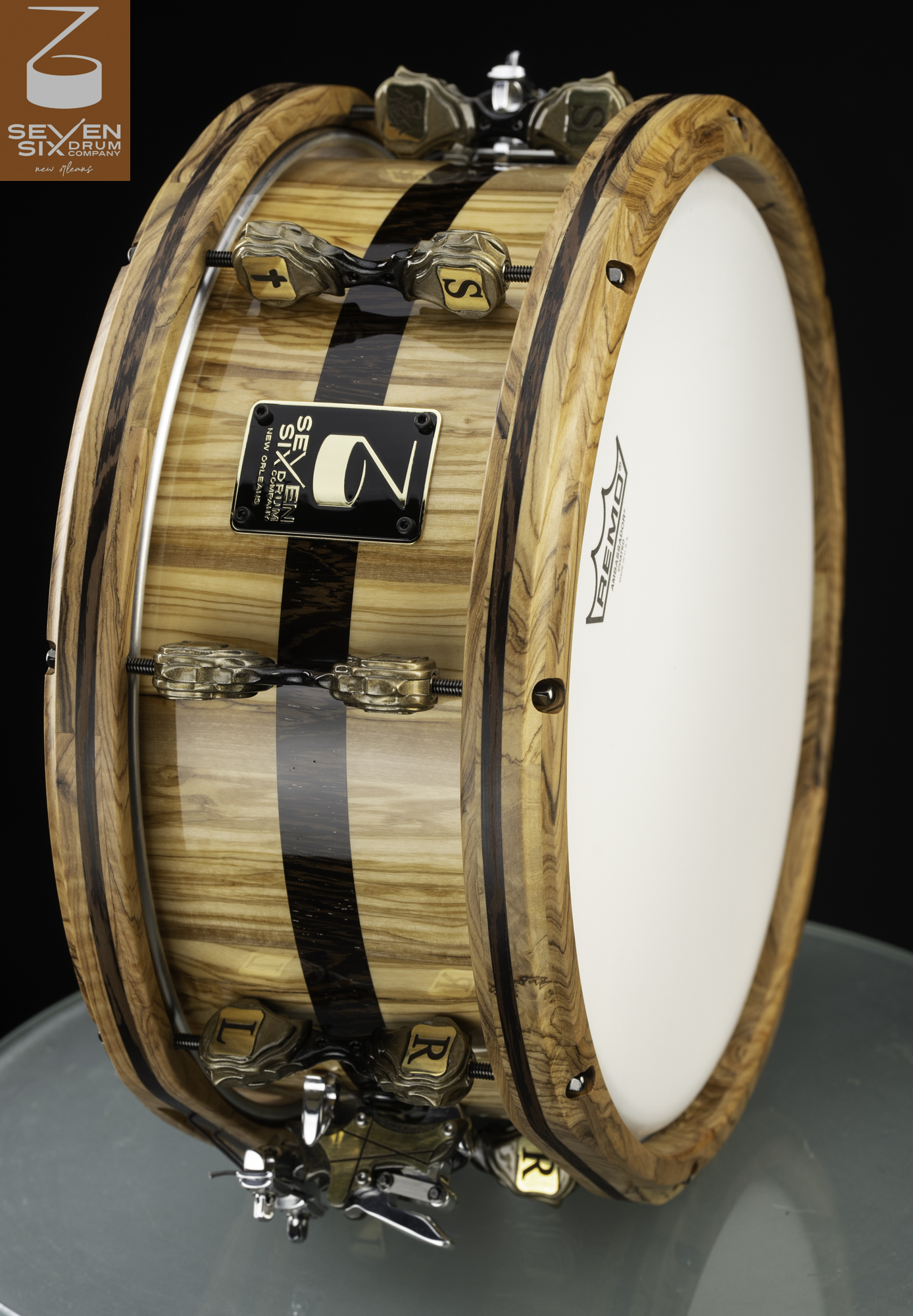 Handcrafted gloss wood snare drum with a dark stripe, matching wooden hoops, and custom bronze lugs.