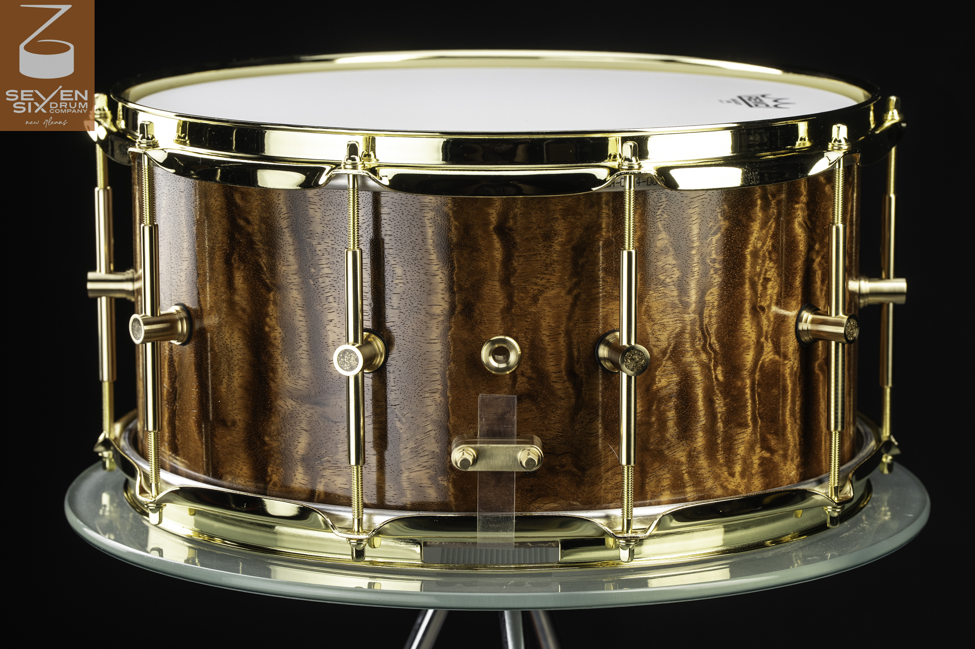 Handmade snare drum with a glossy figured wood shell, polished brass hoops, and tube lugs.