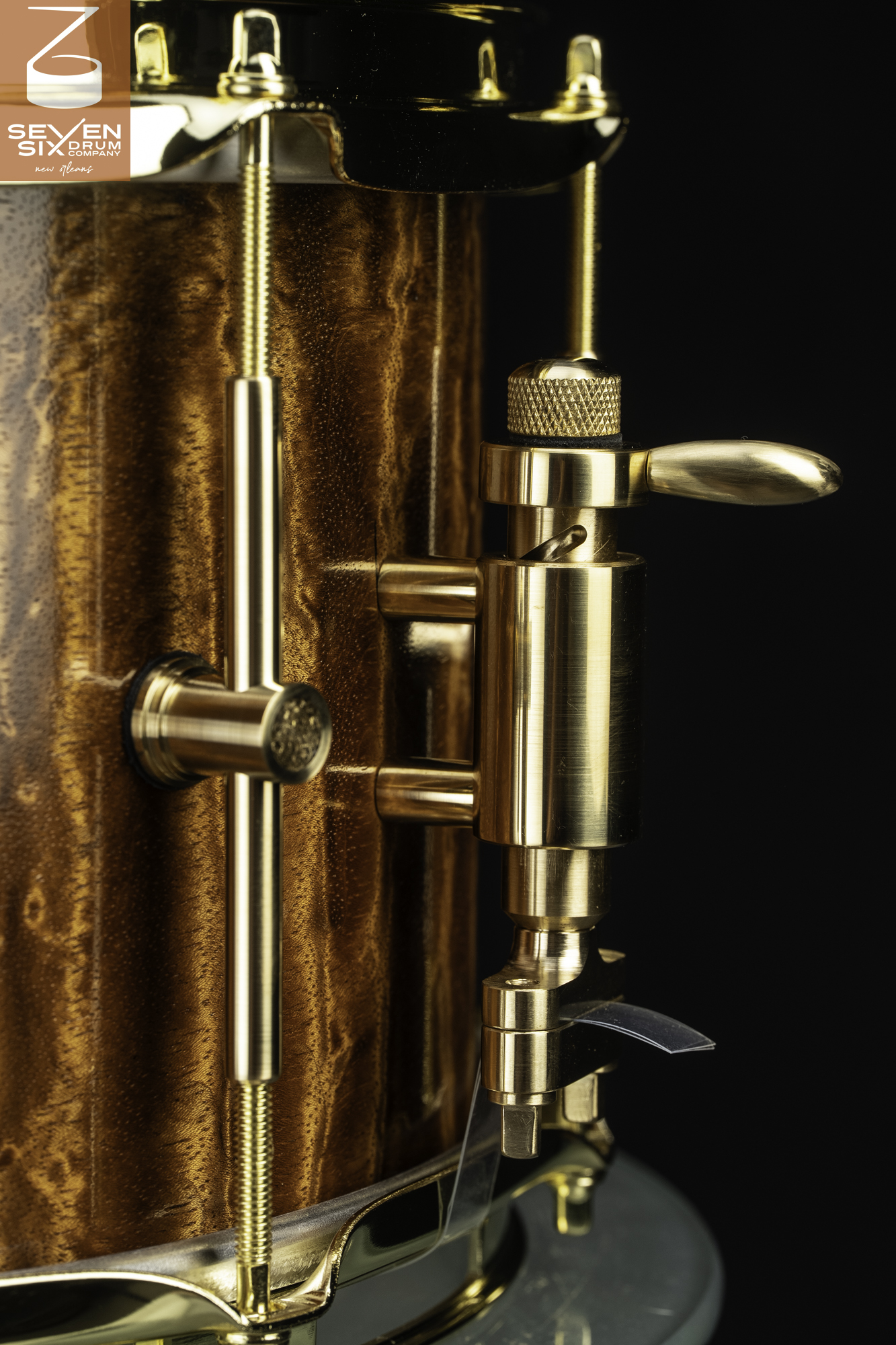 Glossy figured wood snare drum with a polished brass throw-off mechanism and tube lugs.