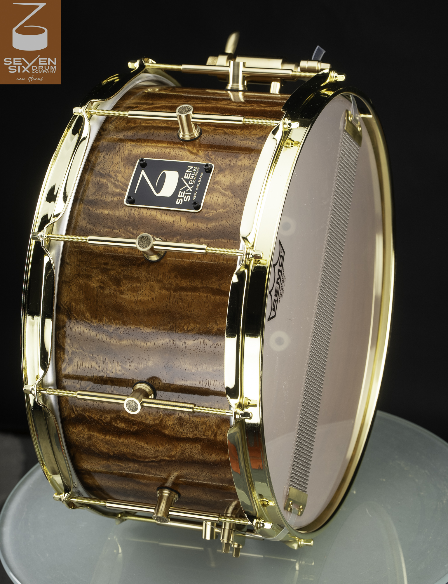Handmade snare drum featuring a high-gloss figured wood shell with polished gold-plated hoops and single-point lugs.