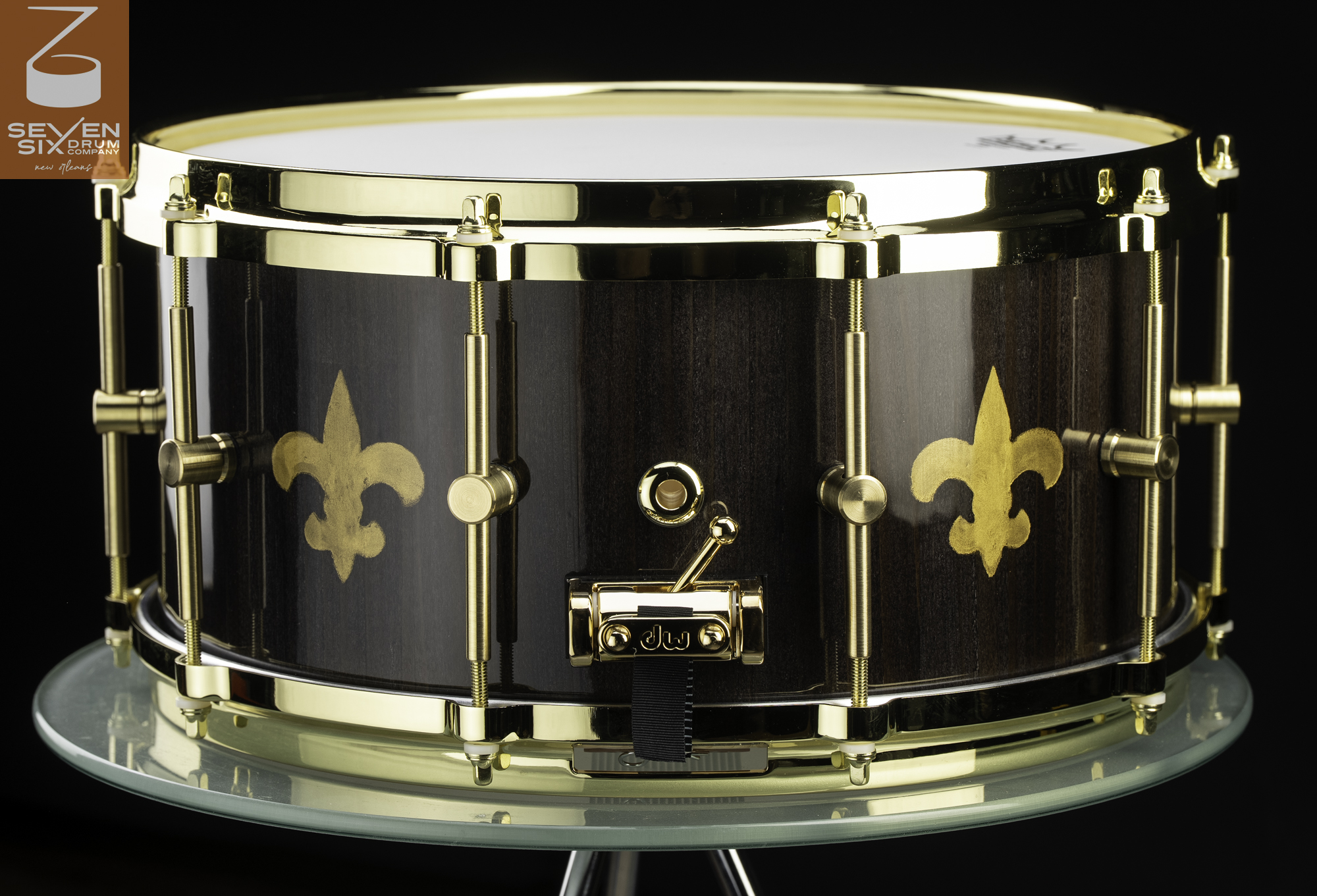 Dark wood snare drum with a glossy finish, gold fleur-de-lis designs, brass tube lugs, and polished gold hardware.