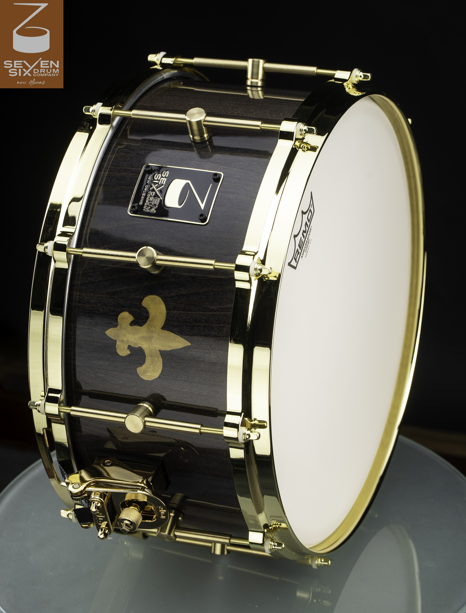 Handmade snare drum with a glossy dark wood shell, gold fleur-de-lis detail, and polished gold hardware and hoops.