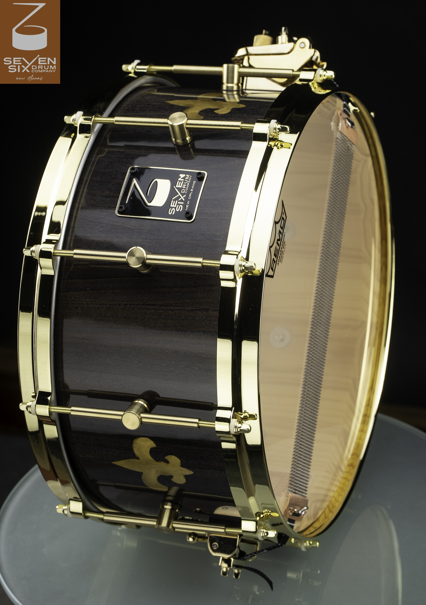 Handmade snare drum featuring a dark wood shell with gold fleur-de-lis inlays, polished gold hoops, and tube lugs.